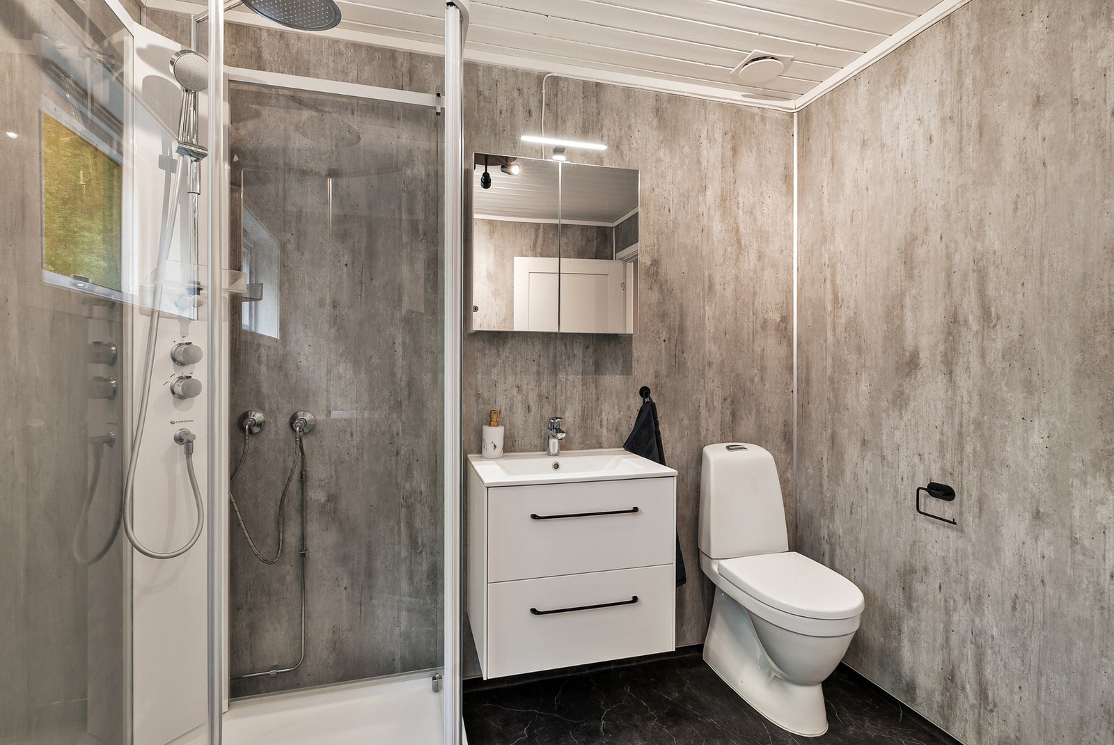 Badet har moderne innredning, speilskap med lys over, dusjkabinett m/regndusj, gulvstående toalett og opplegg for vaskemaskin. Galleribilde
