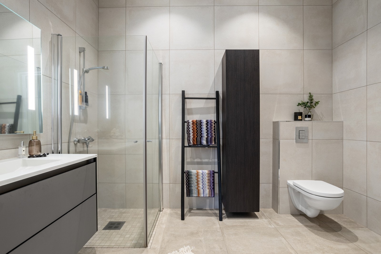 Lyst, pent og flislagt bad, med dusjhjørne, vegghengt toalett og servant med underskap og overspeil - Opplegg til vaskemaskin og tørketrommel. Galleribilde