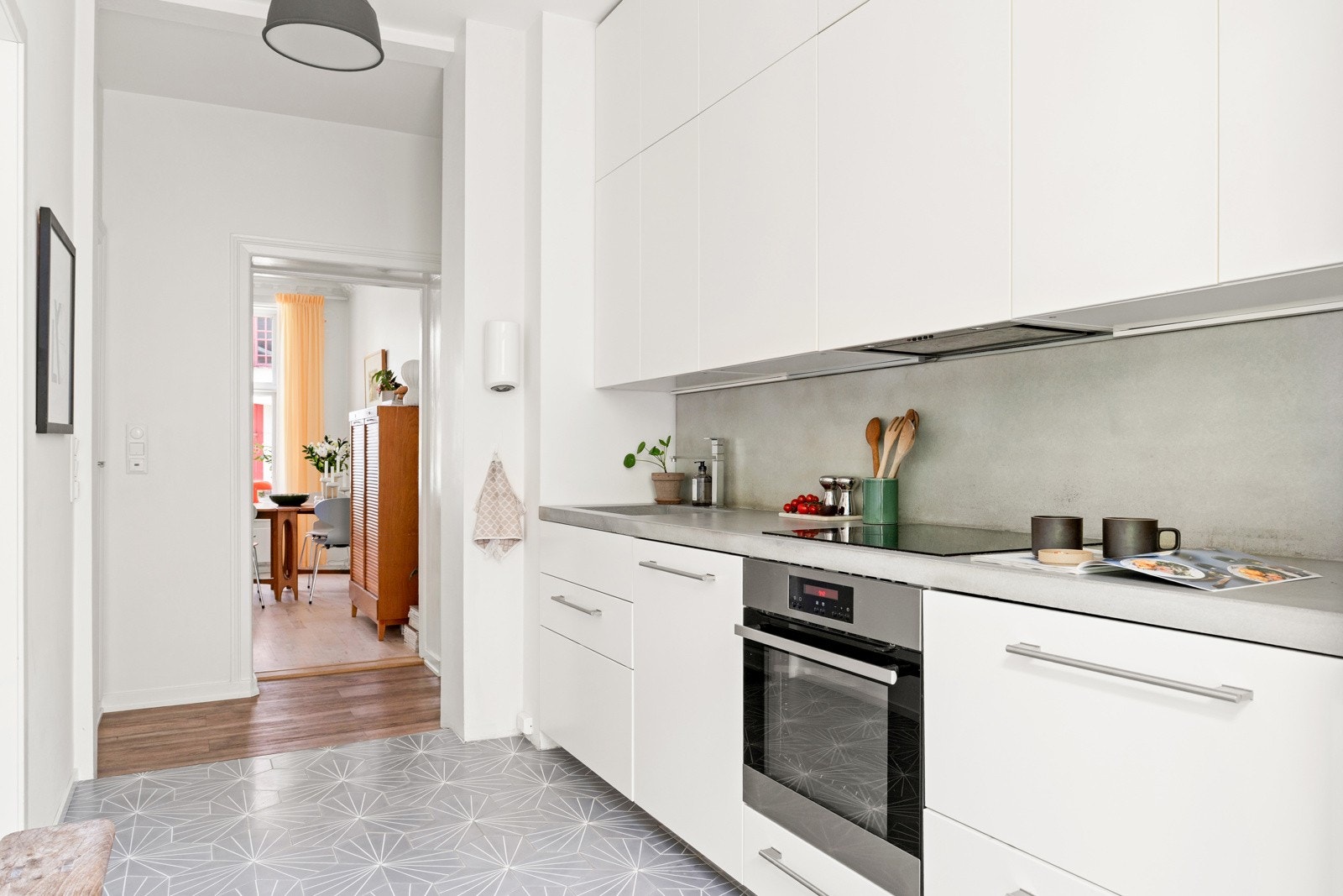 Kjøkkeninnredning fra Ikea med hvite slette fronter, stålhåndtak og overskap med benkebelysning. Benkeplate i betong med støpt vask og ett-greps armatur i krom Galleribilde