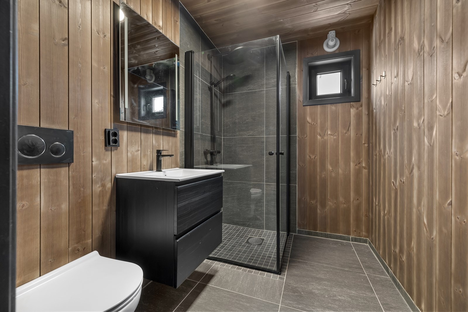 Baderom med store 60x60 gulvfliser, vegghengt toalett og glassdører i dusj. Galleribilde