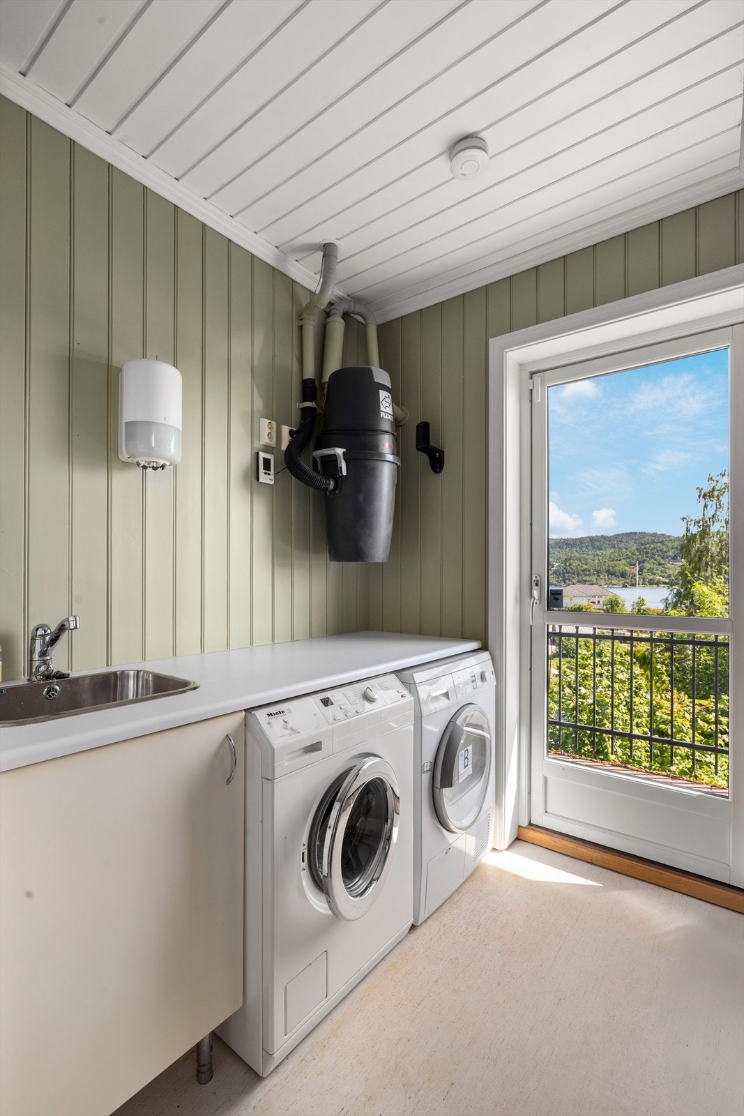 Praktisk vaskerom med opplegg til vaskemaskin og tørketrommel. Vask over skapinnredning. Fra vaskerommet er det utgang til terrasse. Det er montert sentralstøvsuger på vaskerommet Galleribilde