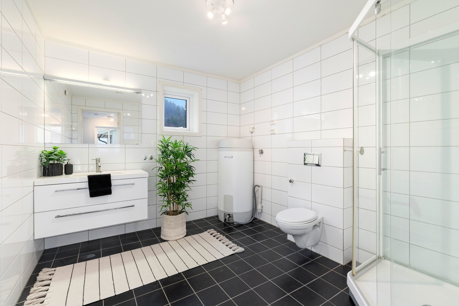 Stilrent kjøkken med blant annet vegghengt toalett, dusjkabinett og baderomsinnredning Galleribilde