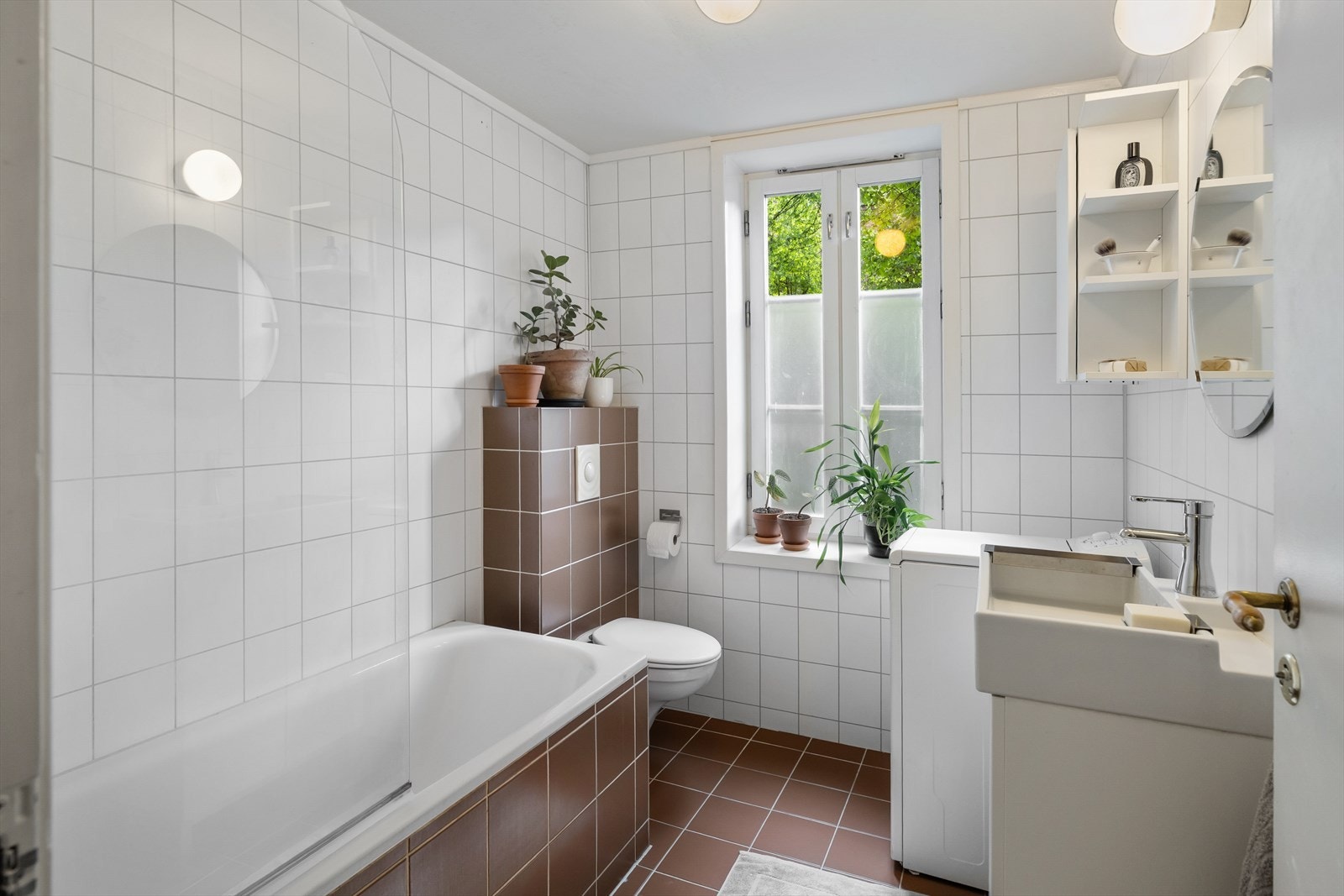 Flislagt bad med wc, baderomsinnredning, badekar og opplegg for vaskemaskin Galleribilde