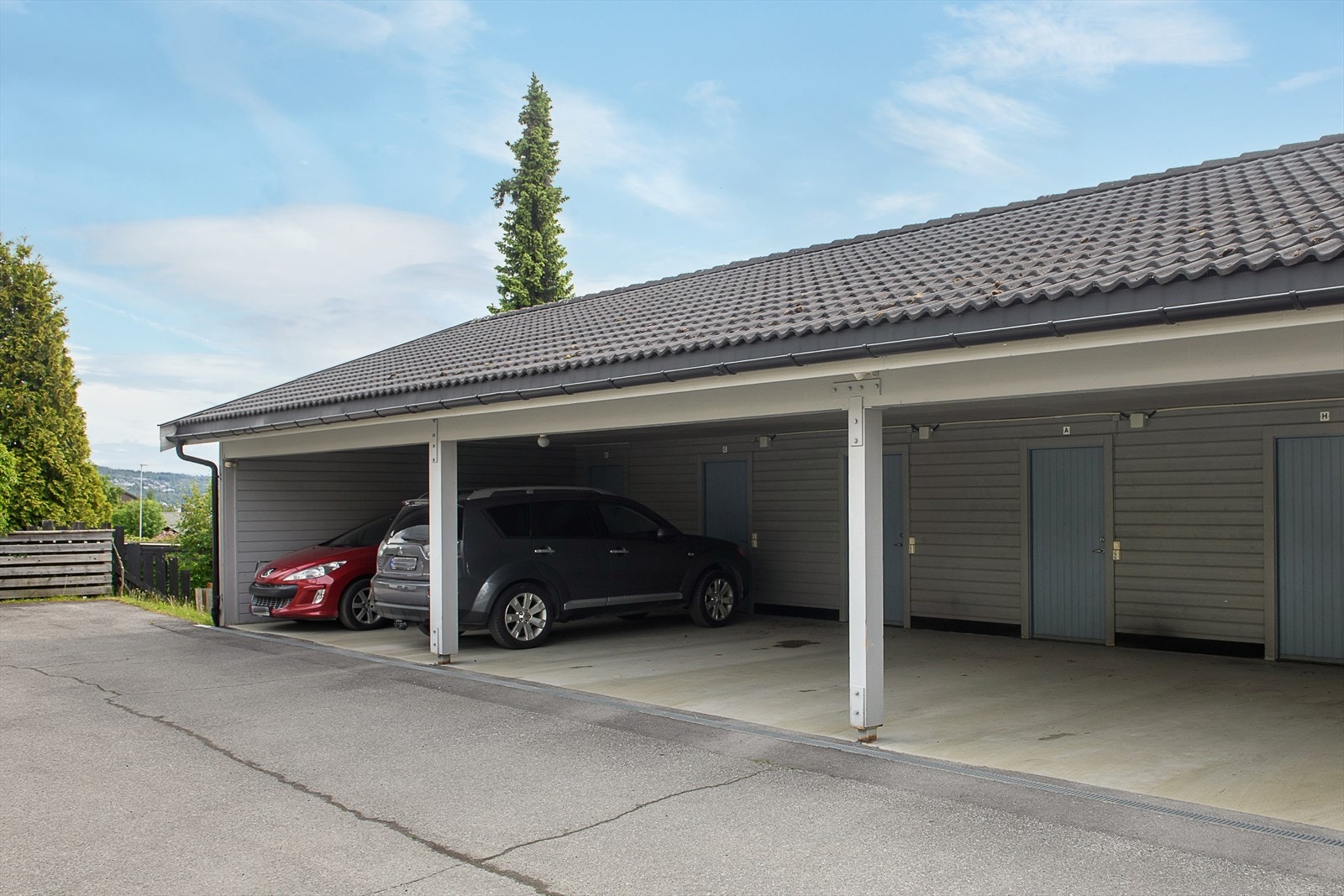 Biloppstillingsplass i carportanlegg med bod i bakkant. Det er lagt opp til elbil-lading, men ladestasjoner er ikke montert. Galleribilde