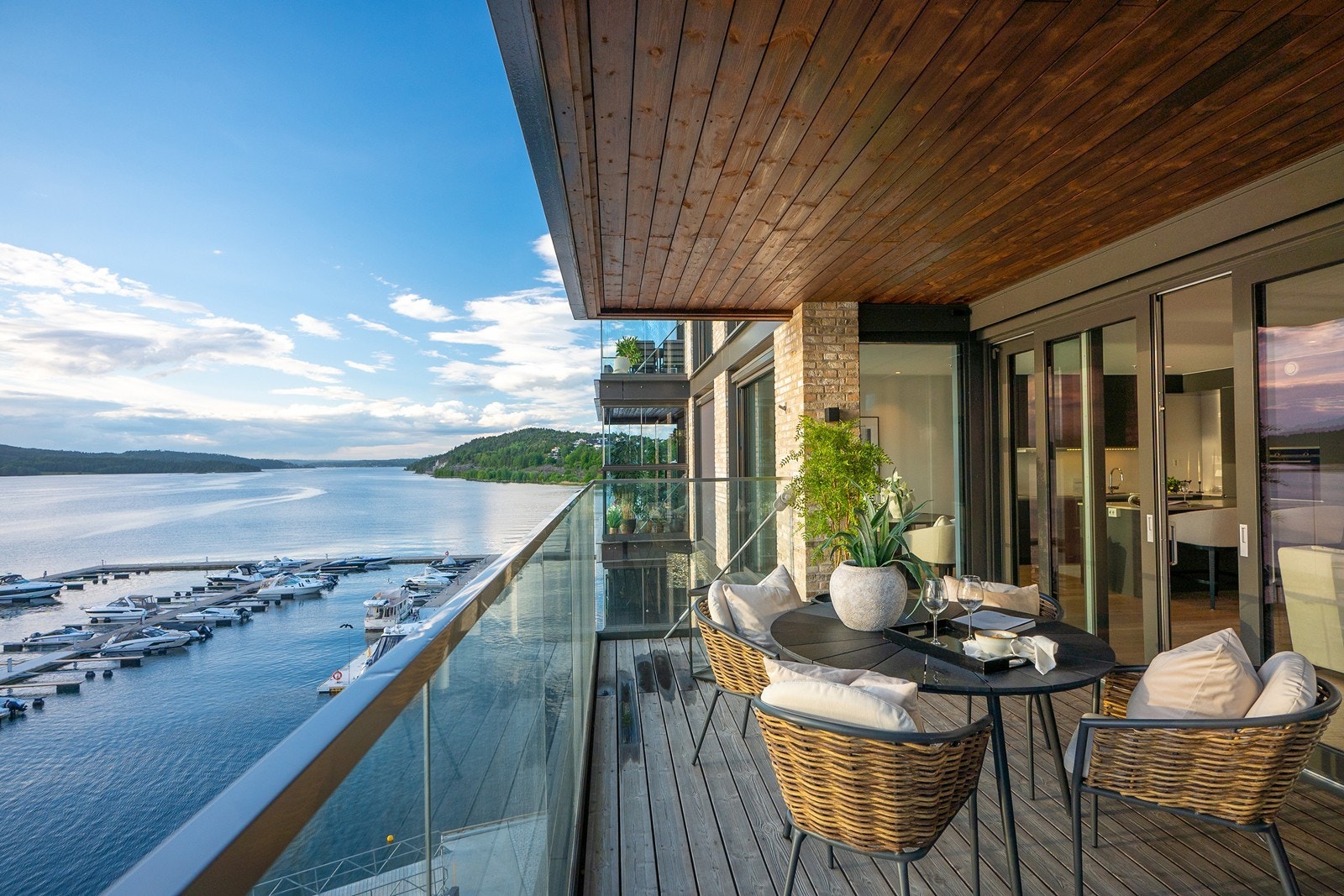 Balkongen har terrassegulv som gir en lun atmosfære, moderne glassrekkverk og god plass til både spisegruppe og loungemøbler. Galleribilde