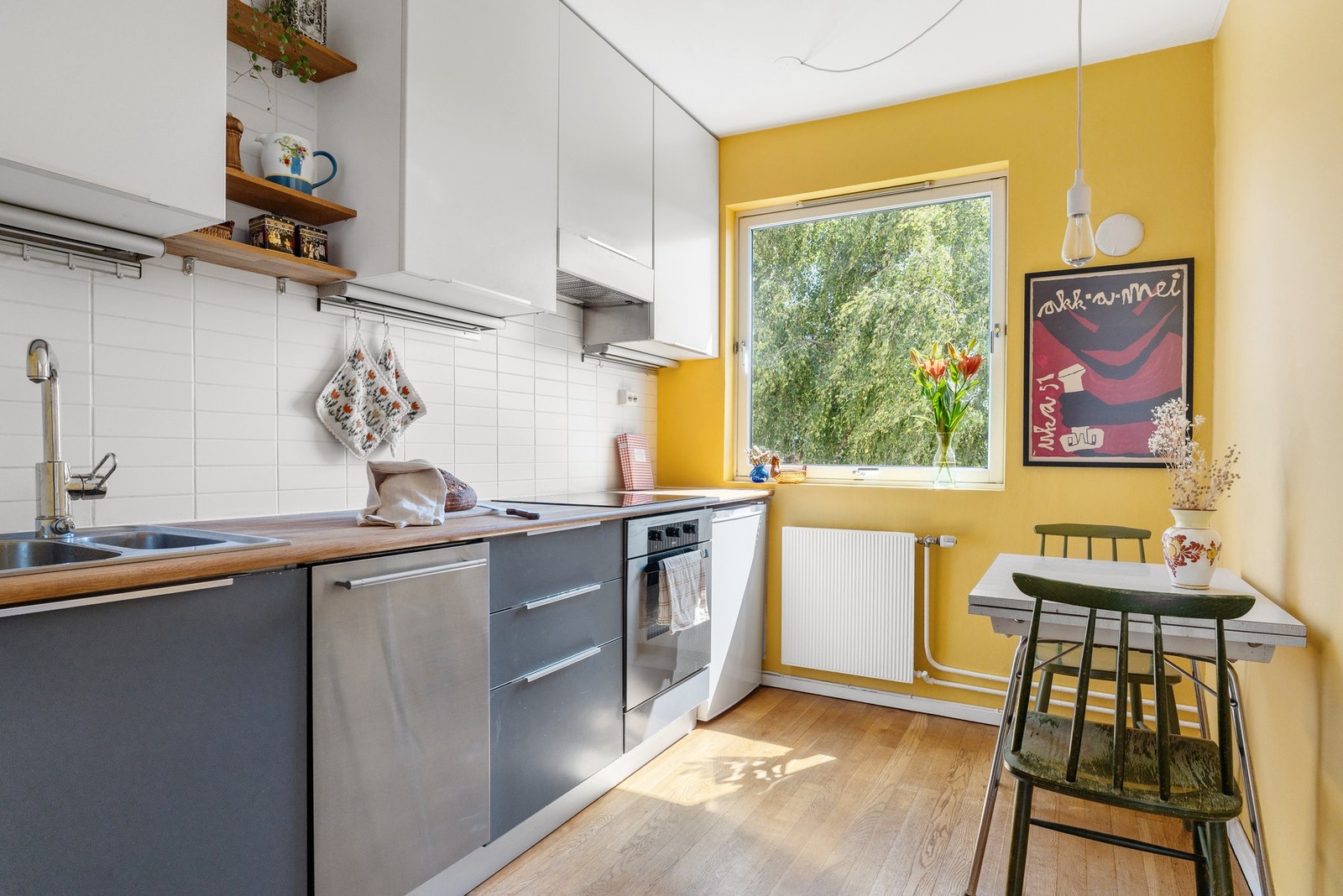 Innbydende kjøkken med moderne innredning med slette fronter og heltre benkeplate. Praktiske og dekorative detaljer som flislagt vegg bak benk, overskap med belysning og åpne hyller gir en god kombinasjon av funksjon og design. Galleribilde