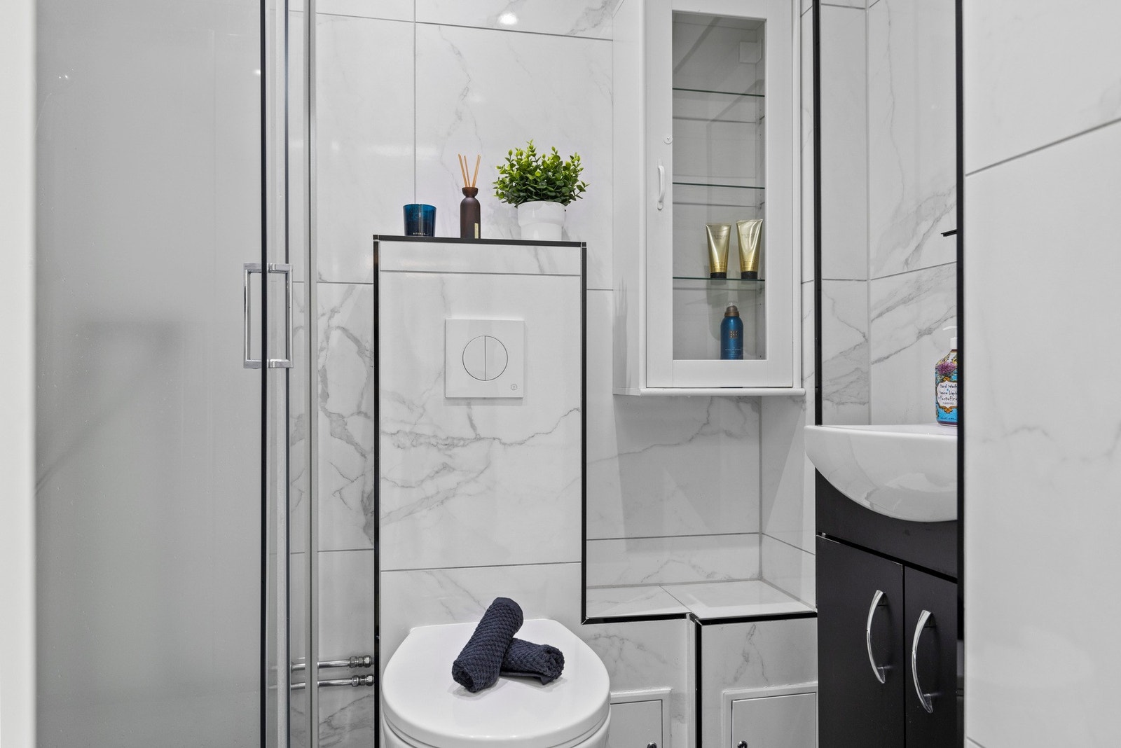 Innredningen inkluderer servant med slette fronter, speil, veggmontert skap, dusjkabinett og vegghengt toalett Galleribilde