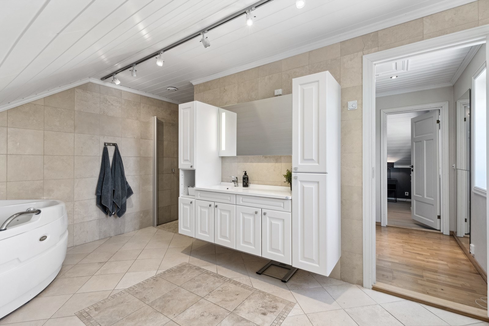 Pent flislagt baderom med hjørnebadekar, toalett og dusjnisje. Galleribilde