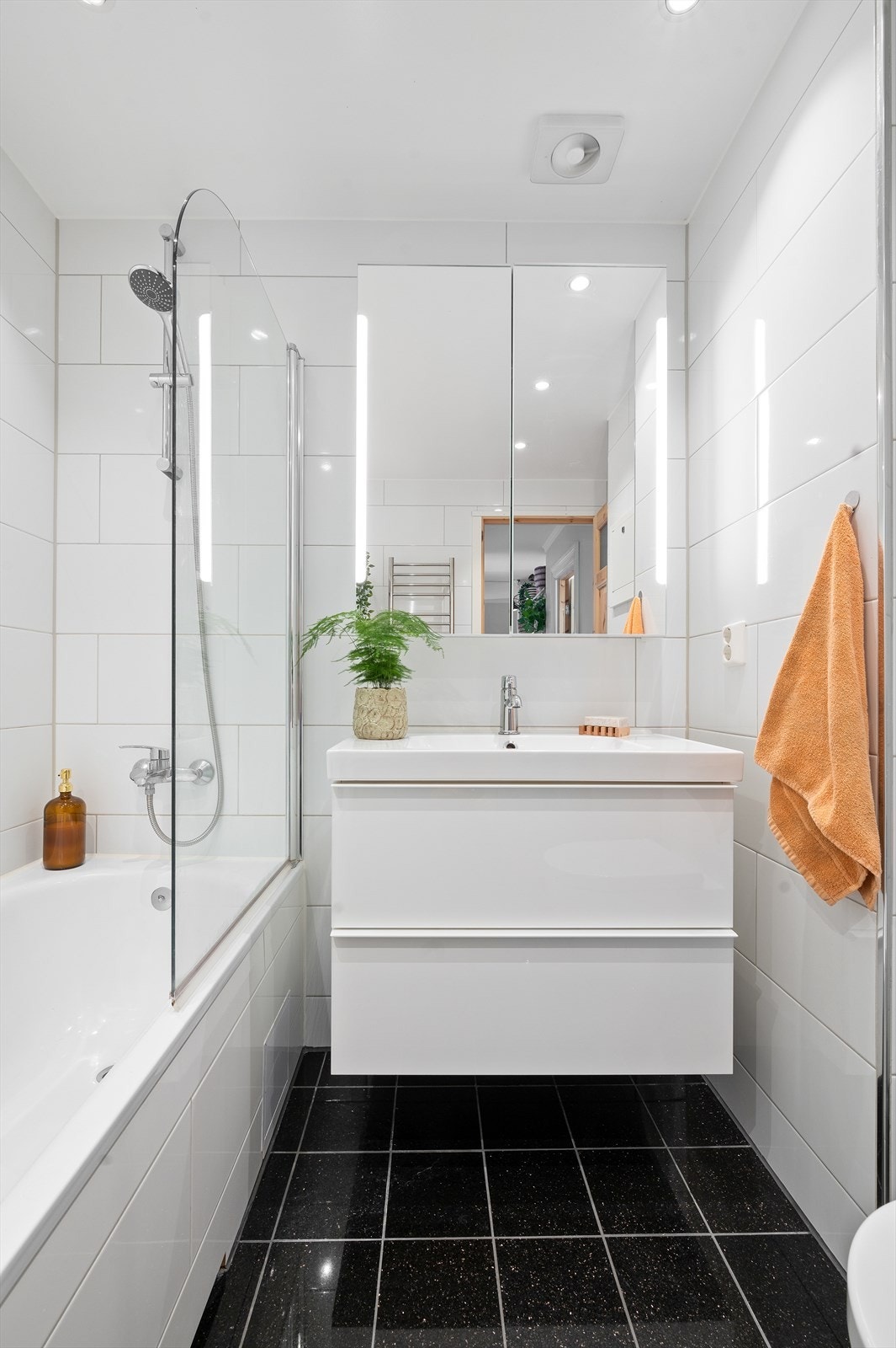 Over servanten er det et vegghengt speilskap med integrert lys og stikkontakter. Videre har badet et innmurt badekar med dusjvegg og vegghengt toalett. Galleribilde