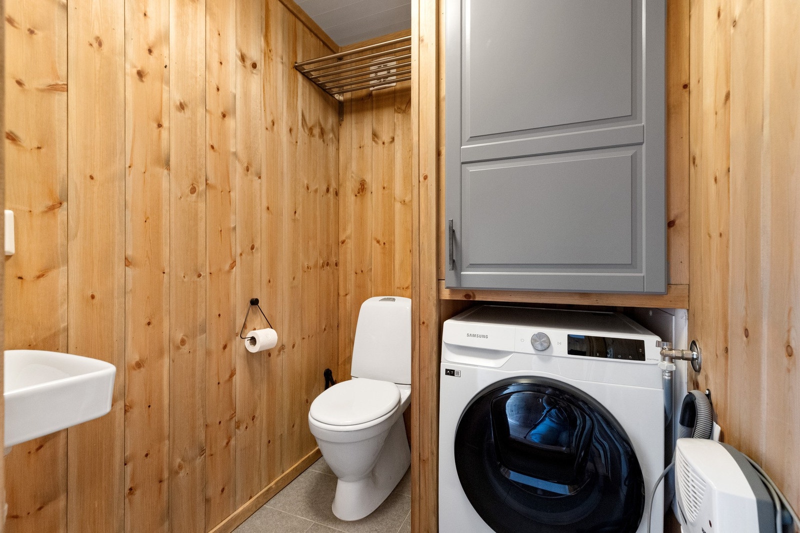 Eget toalettrom med opplegg til vaskemaskin. Skap over vaskemaskin for oppbevaring av rengjøringsmidler etc.
Fliser og varmekabler på gulv. Skotørker plassert på vegg Galleribilde