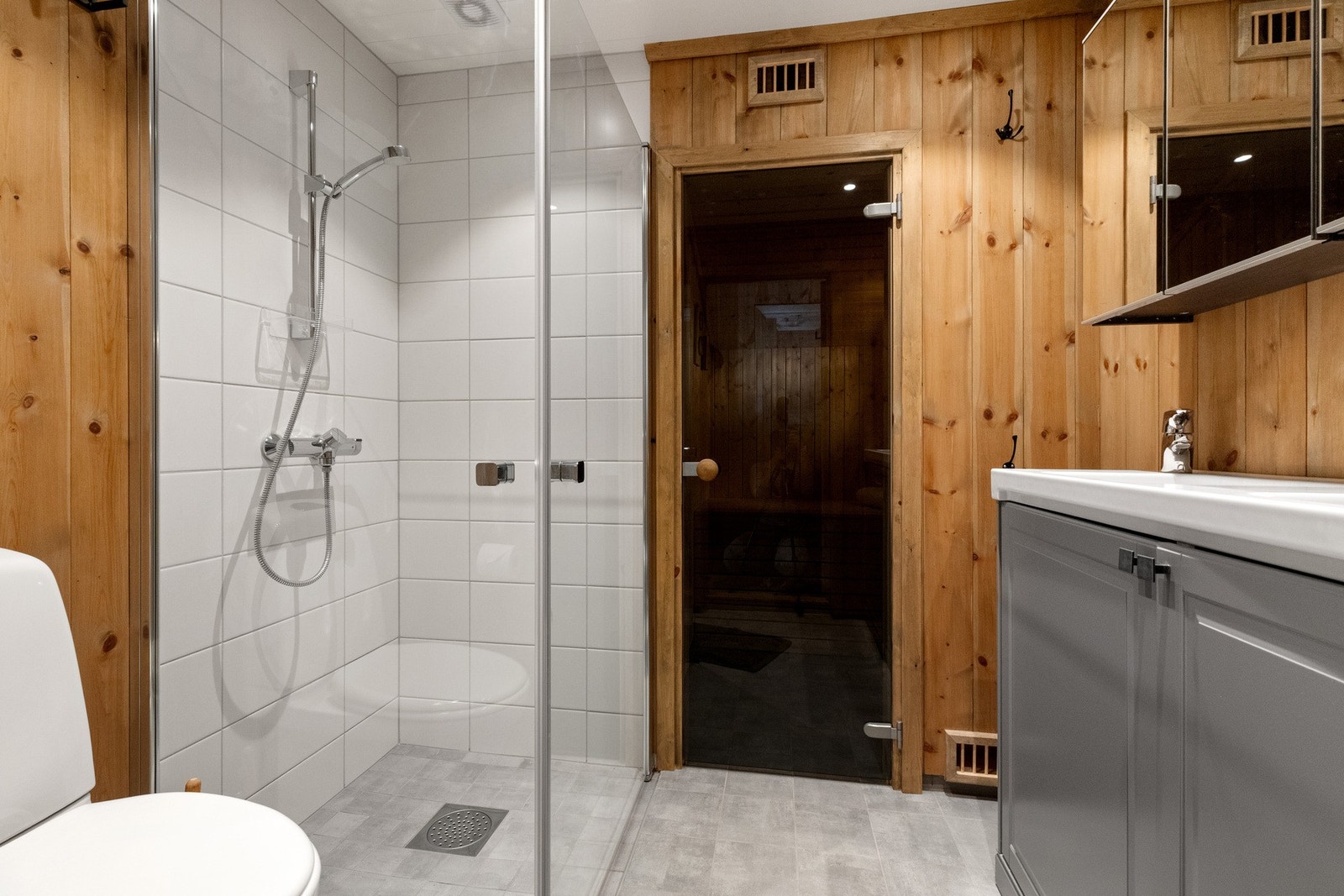 Badet har fliser og varmekabler på gulv. Panel på vegger med unntak i dusjnisje hvor det er hvite fliser Galleribilde