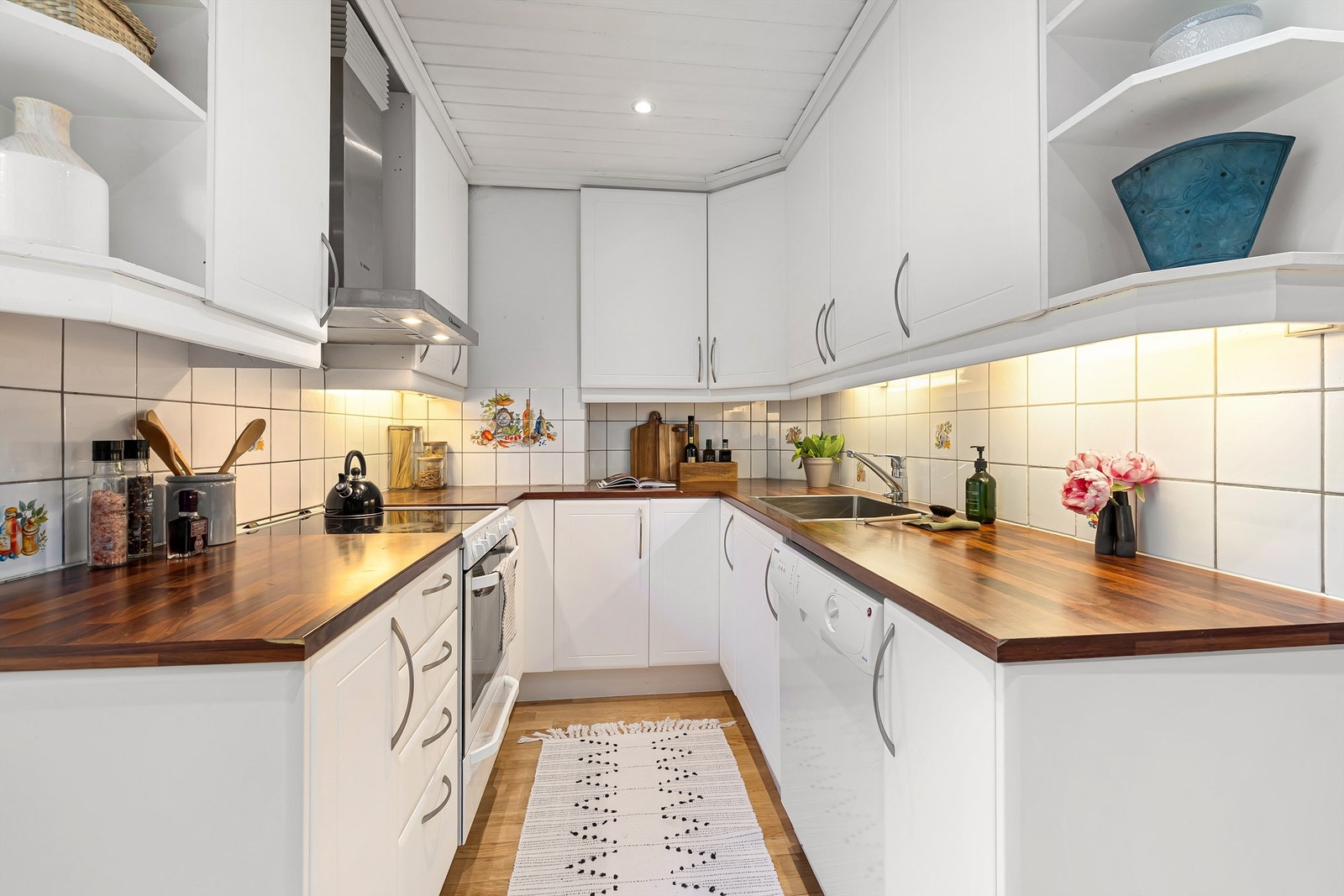 Kjøkkenet har profilerte fronter, fliser mellom laminat benkeplate og overskap, benkeskapsbelysning og stikkontakter under overskap og nedfelt oppvaskkum med ett-greps blandebatteri. Galleribilde