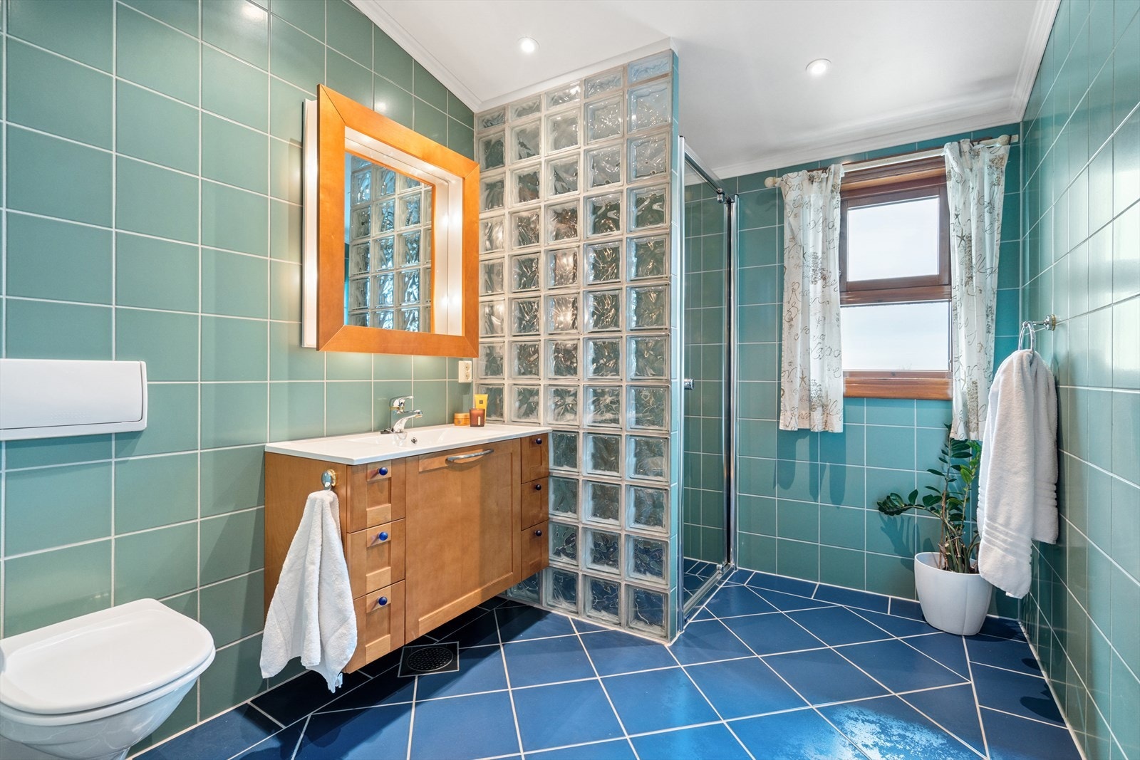 Badet er utført med flislagte overflater i spreke farger - Her finner du vegghengt toalett, dusjhjørne m/glassbyggerstein og baderomsinnredning Galleribilde