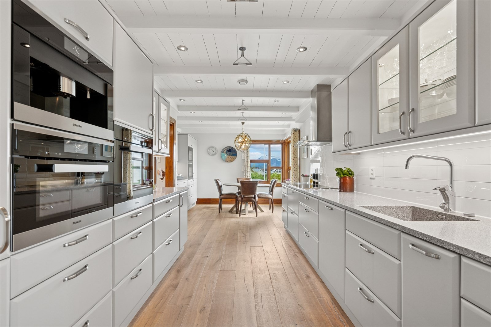 Stilren kjøkkeninnredning fra 2020 levert av Nygård kjøkken - Det er malte glatte fronter, Corian benkeplate med nedfelt kjøkkenvask og fliser på vegg over benk Galleribilde