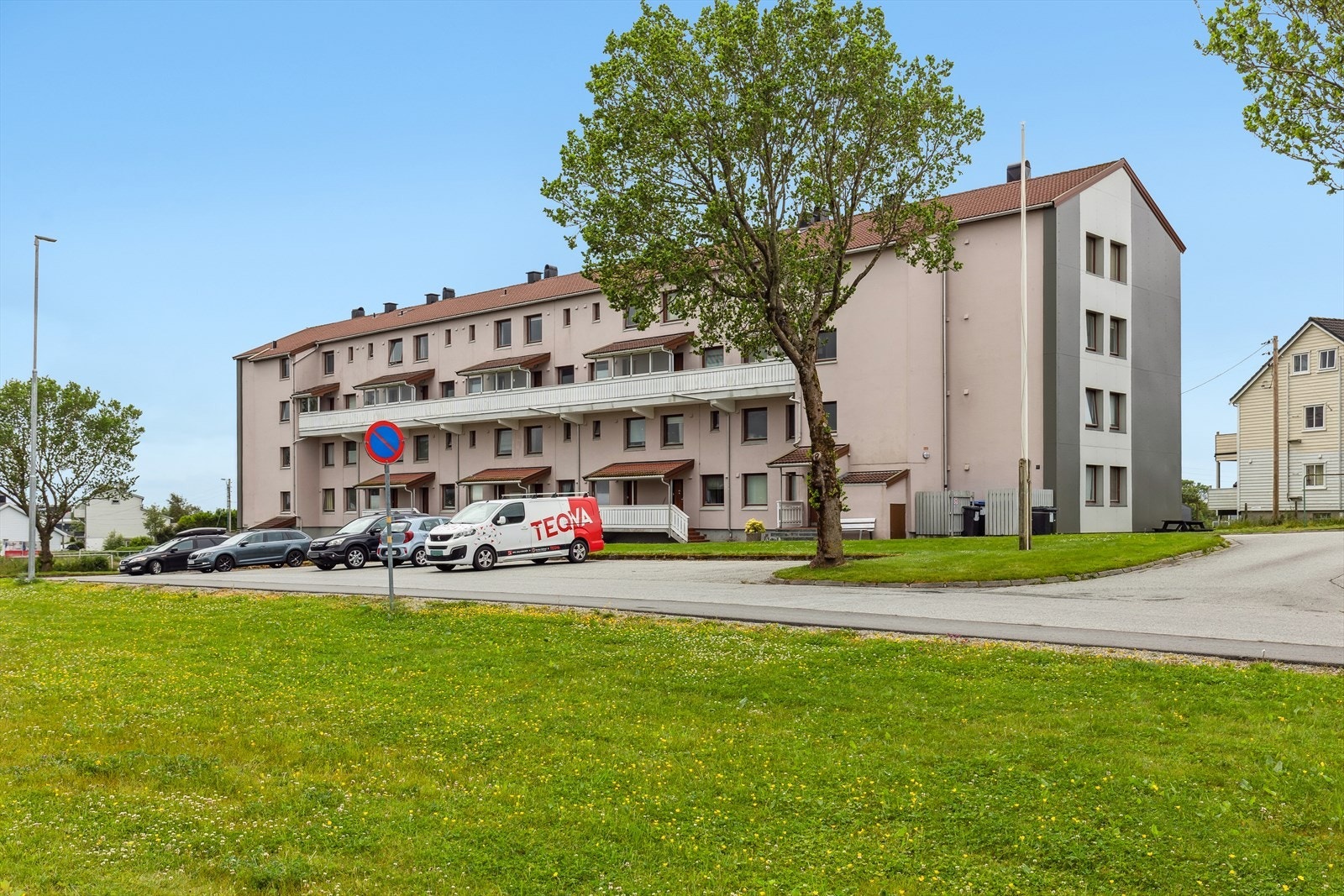 Pent opparbeidet med plen, prydbusker og benker, samt asfaltert parkeringsplass beliggende foran blokken. Galleribilde