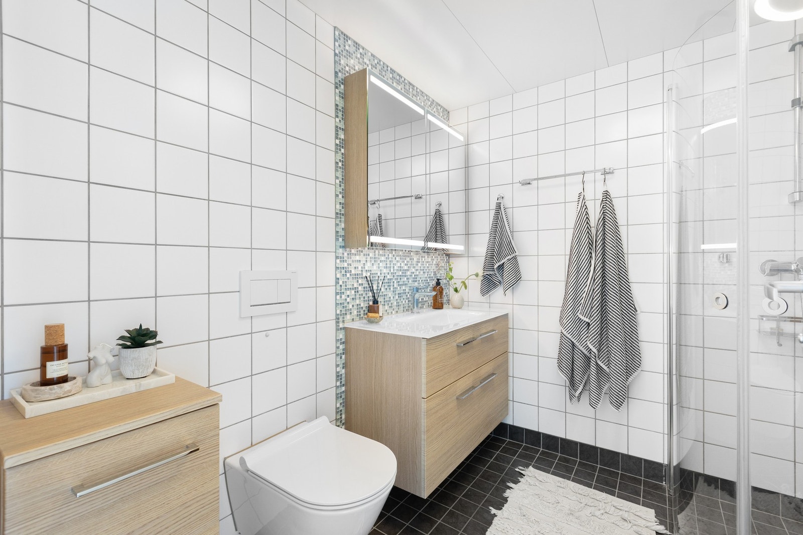 Delikat baderom med flislagt gulv med gulvvarme og lyse delikate fliser på veggene. Galleribilde