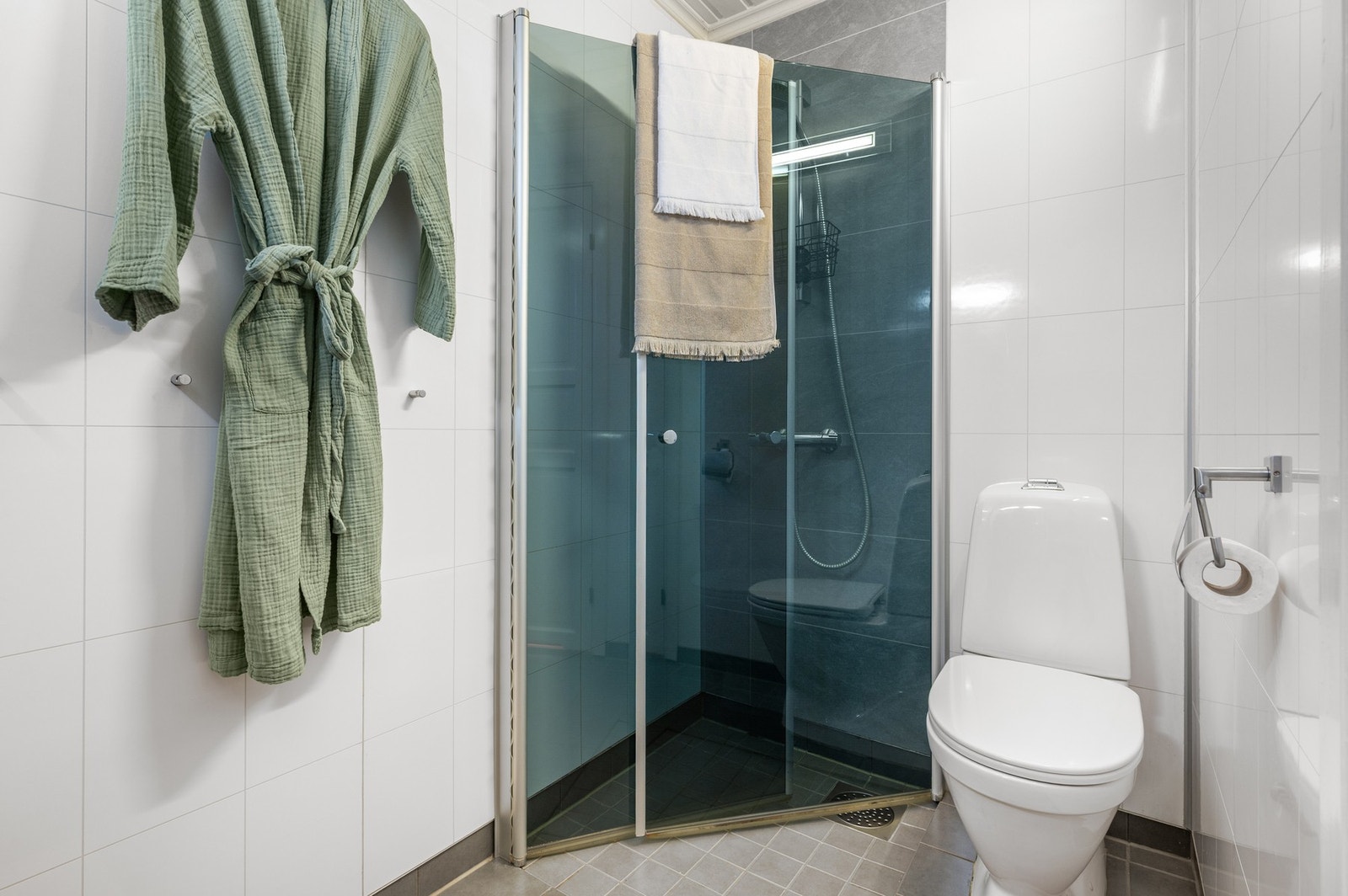 Flislagt bad med dusjhjørne, toalett og opplegg for vaskemaskin. Galleribilde