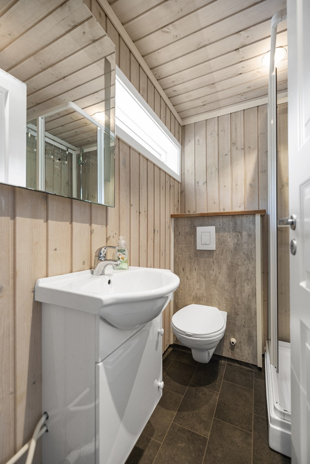 Badet i leiligheten er innredet med servantinnredng med skap, speil, vegghengt toalett, dusjkabinett og opplegg til vaskemaskin Galleribilde