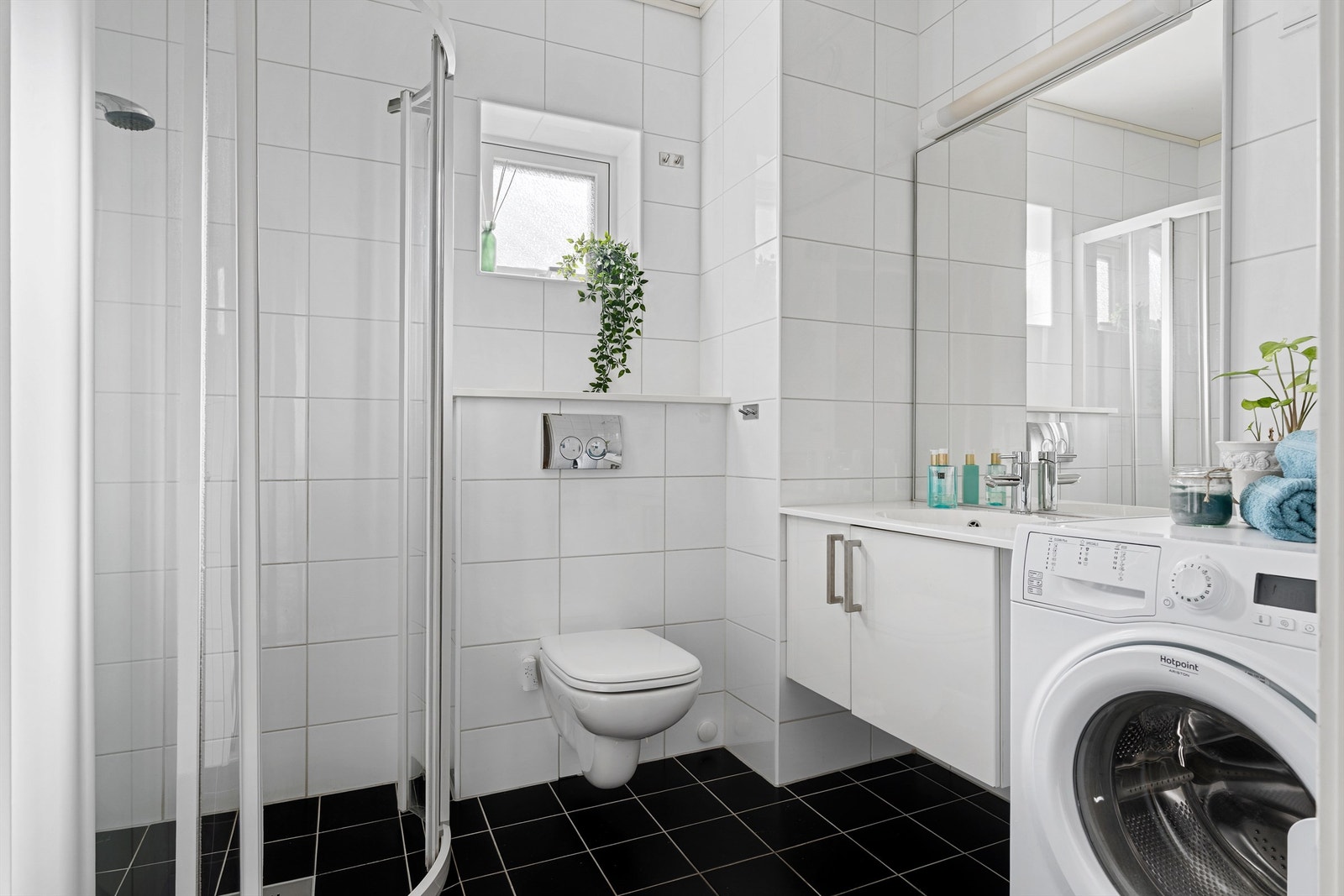 Pent flislagt bad utstyrt med vegghengt toalett, servantskap med speil og lys, dusjhjørne og opplegg for vaskemaskin. Galleribilde