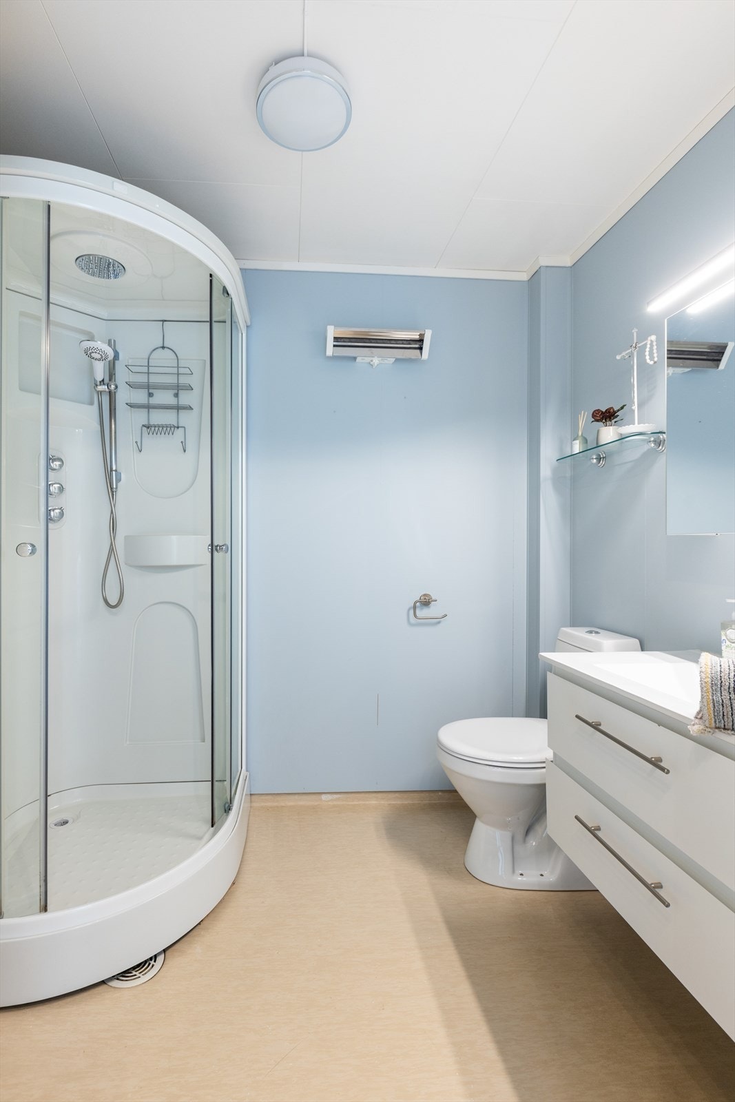 Badet er utstyrt med dusjkabinett, toalett, heldekkende servant med skuffer og speilskap. Galleribilde