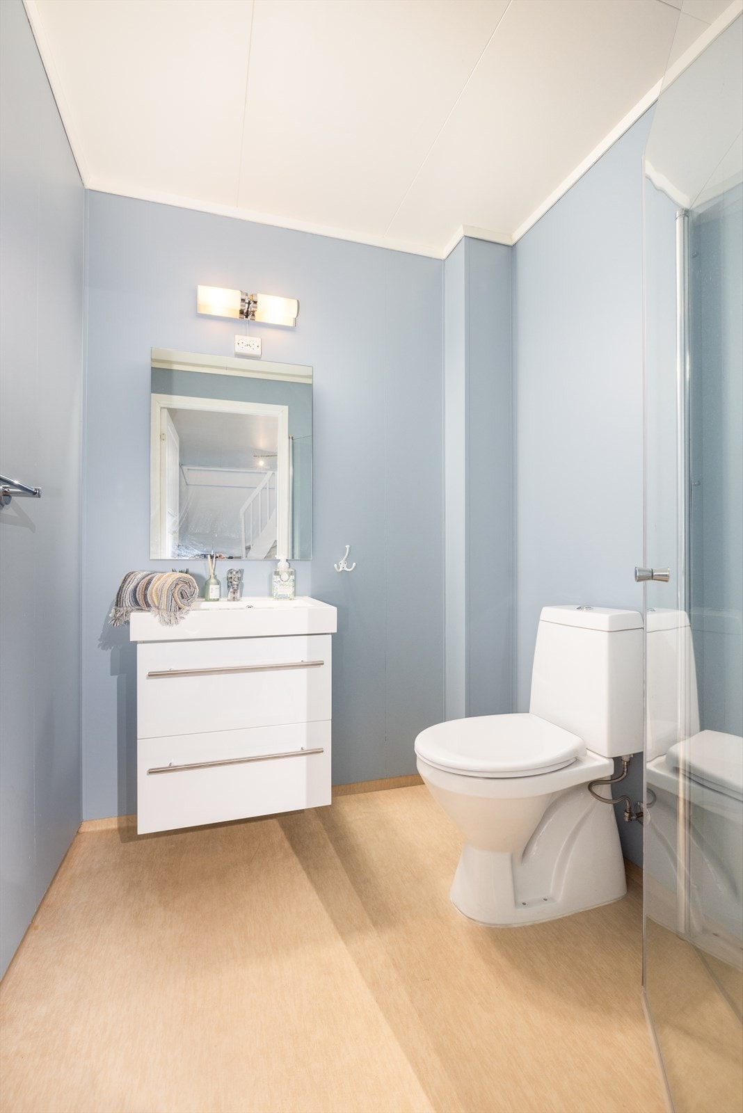 Badet i underetasjen har malte baderomsplater, vinyl på gulv og takess i himling. Det er elektriske varmekabler i gulvet. Badet er utstyrt med dusj med glassdører, dusjgarnityr, servant med skuffer og toalett Galleribilde