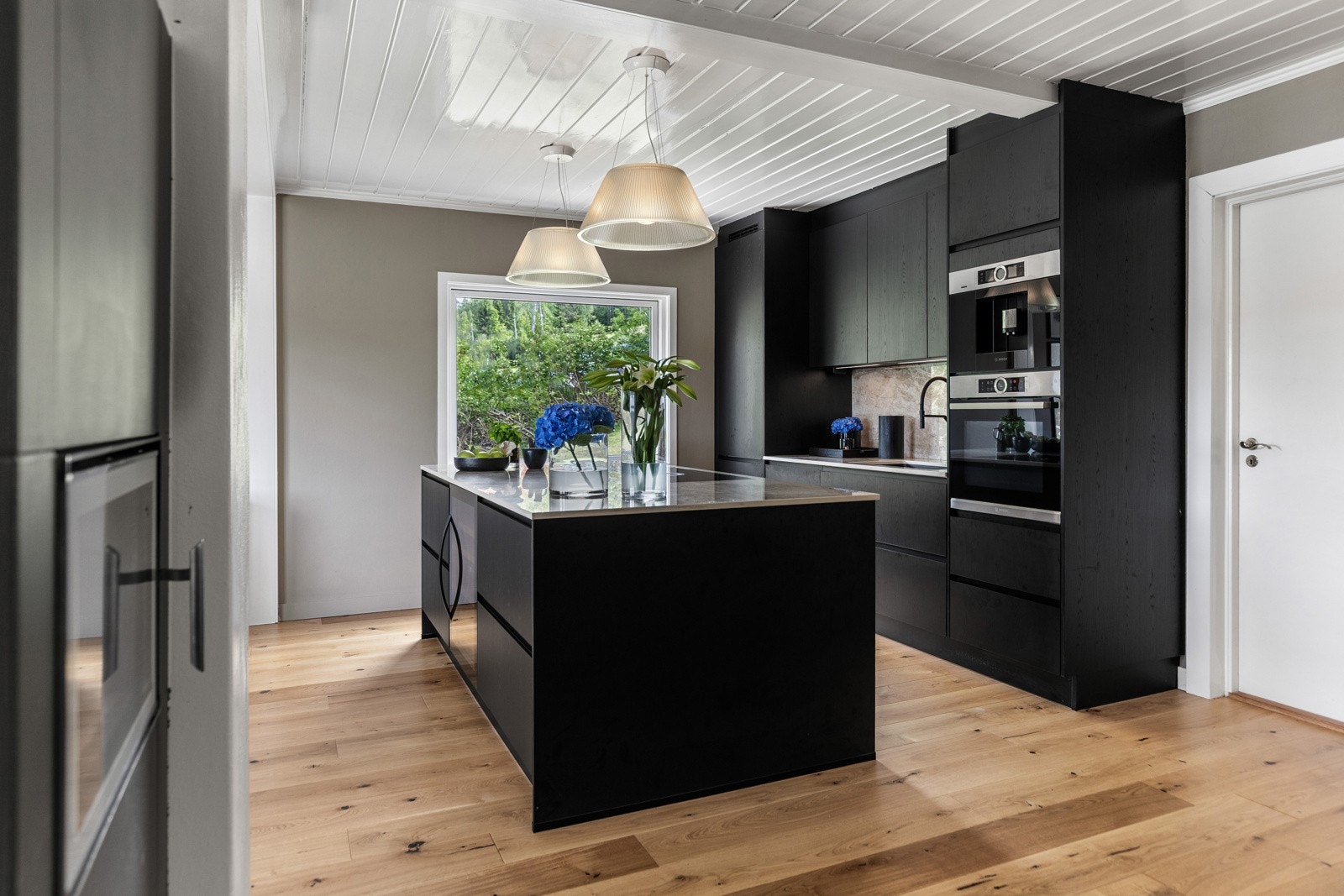 Moderne kjøkken med sorte fronter, kjøkkenøy, integrerte hvitevarer og store vinduer som gir godt med naturlig lys. Galleribilde