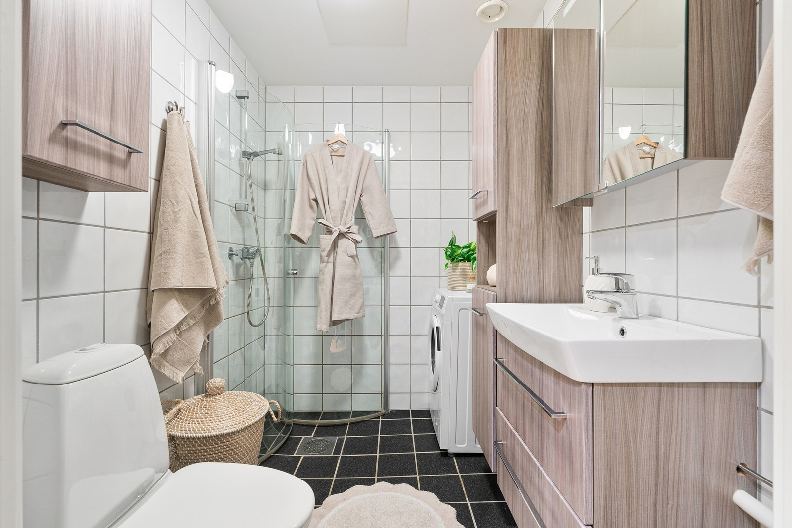 Lyst bad med moderne innredning, dusjhjørne med glassdører, samt opplegg for vaskemaskin. Galleribilde