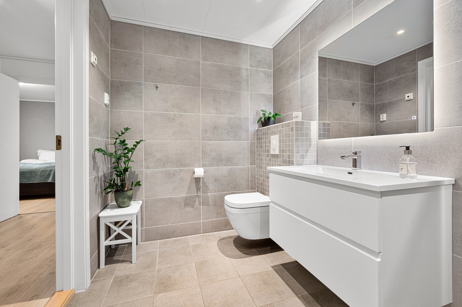 Badet er innredet med plassbesparende dusjdører i glass og veggmontert WC. I himling har du dimbare spotter. Galleribilde