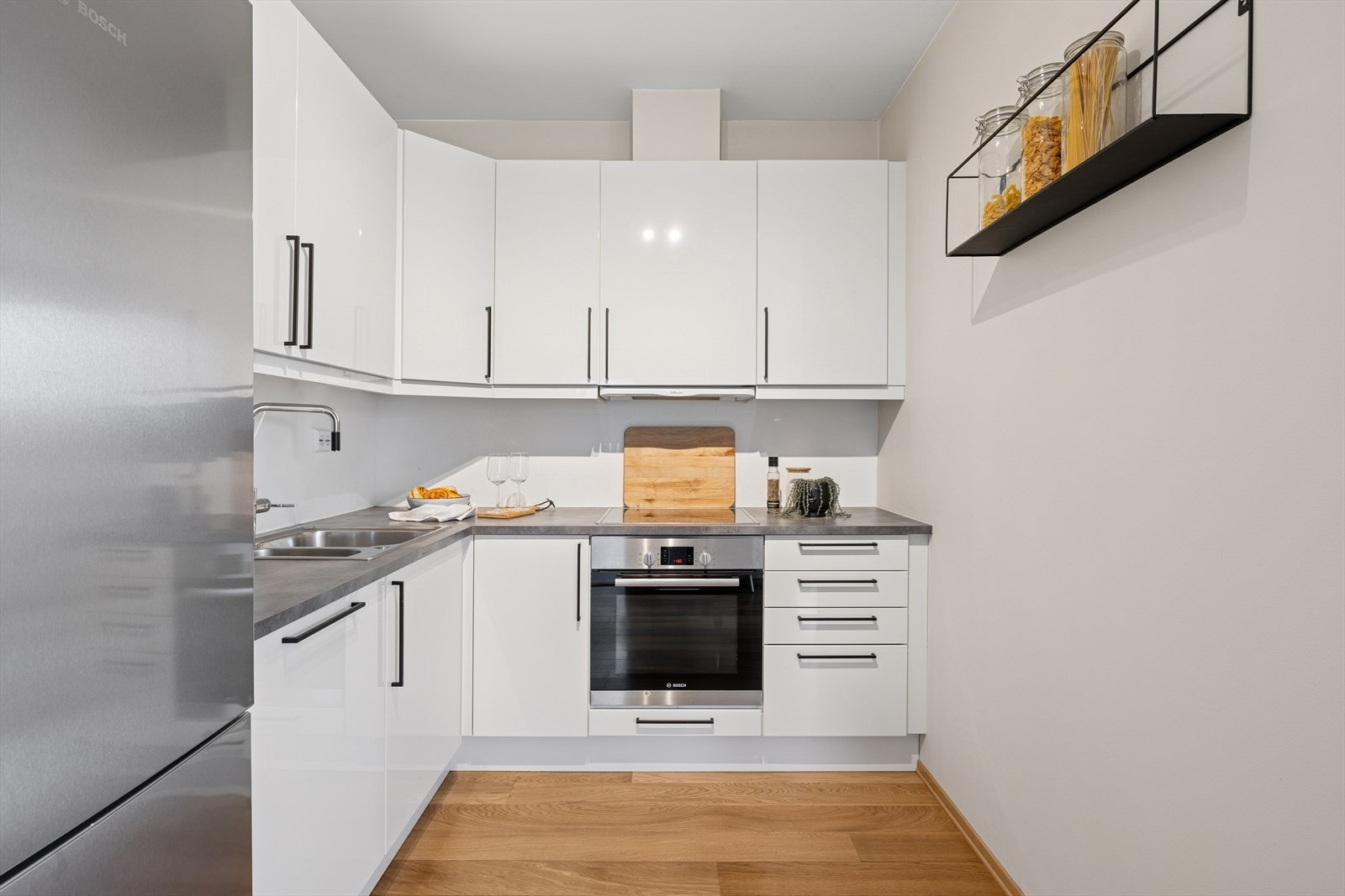 Pen kjøkken med godt med benke- og skapplass, hvite høyglans fronter og grå laminert benkeplate. Galleribilde