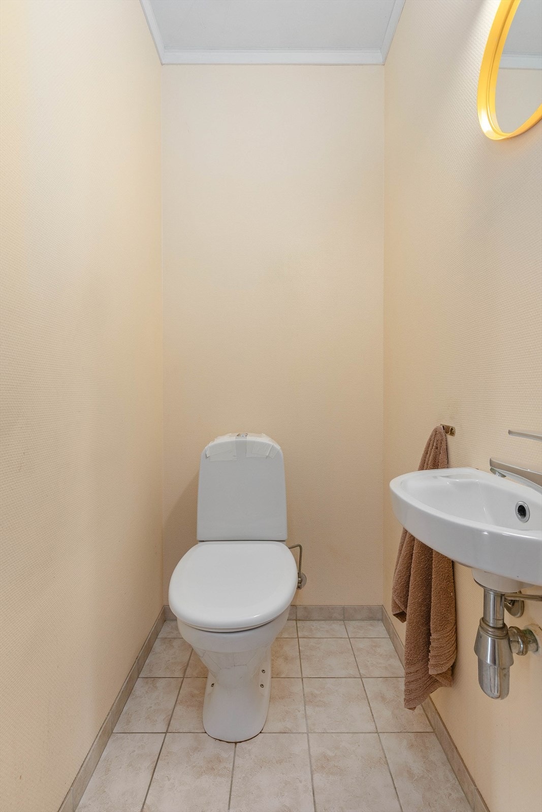 Toalettrom med flis på golvet og malte strier på vegger. Det er toalett og vegghengt servant på rommet. Galleribilde