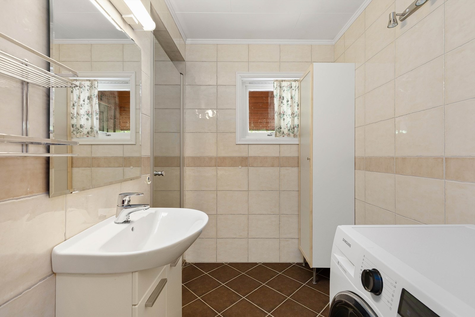 Badet har veggar med fliser, taket har himlingsplater og golvet er fliser med elektriske varmekabler. Rommet har innredning med nedfelt
servant, dusjvegger/hjørne og opplegg for vaskemaskin. Galleribilde