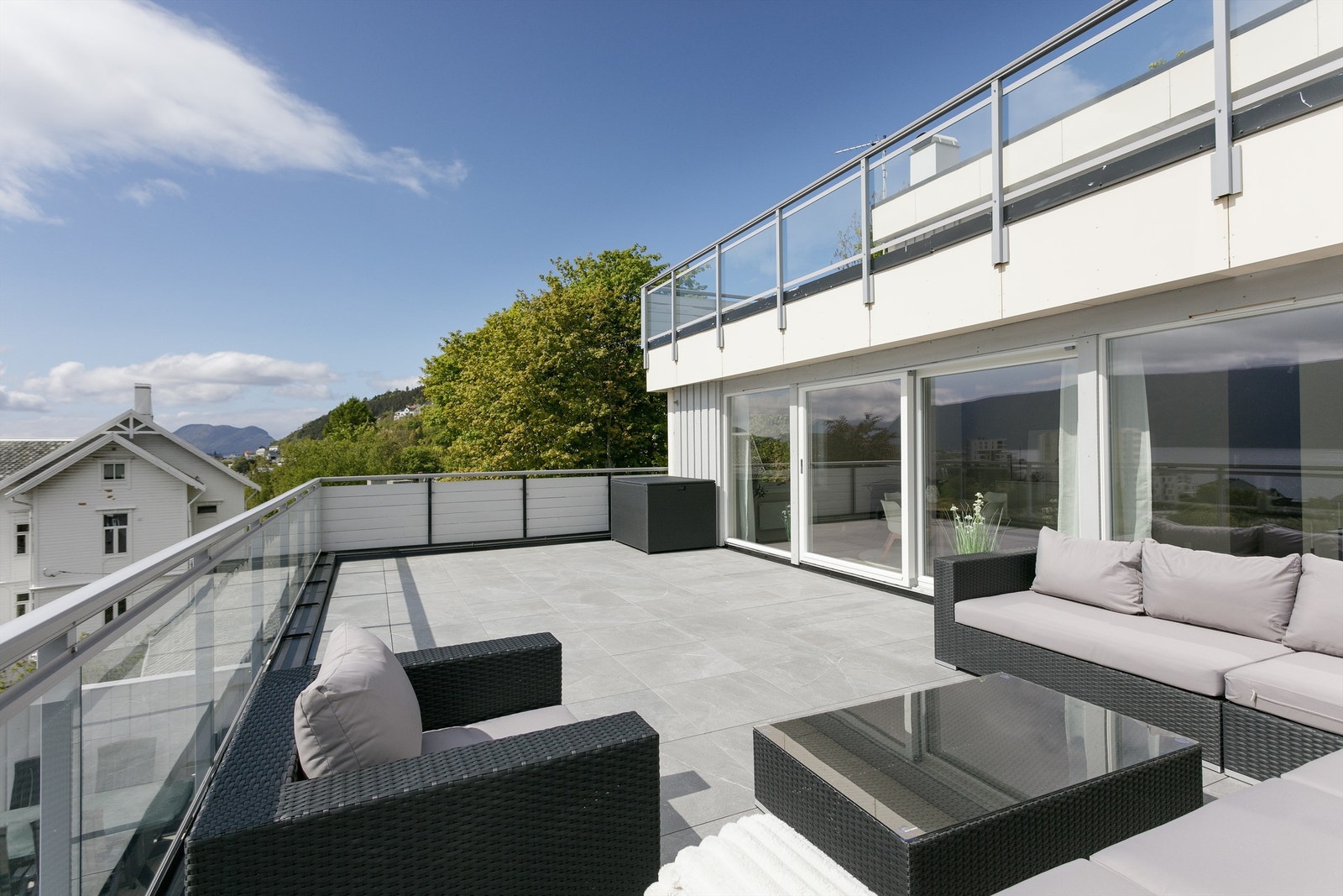 Stor og romslig terrasse med glassrekkverk og god plass til flere soner og sitteplasser Galleribilde