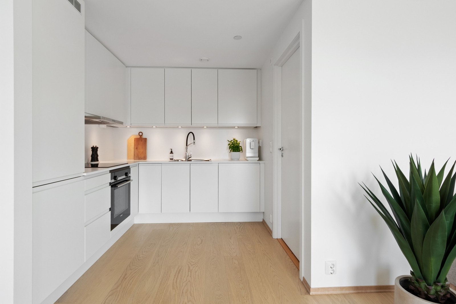 Innredningen er stilren og moderne, med hvite, glatte fronter og dobbel oppvaskkum nedfelt i en hvit benkeplate av laminat. Galleribilde