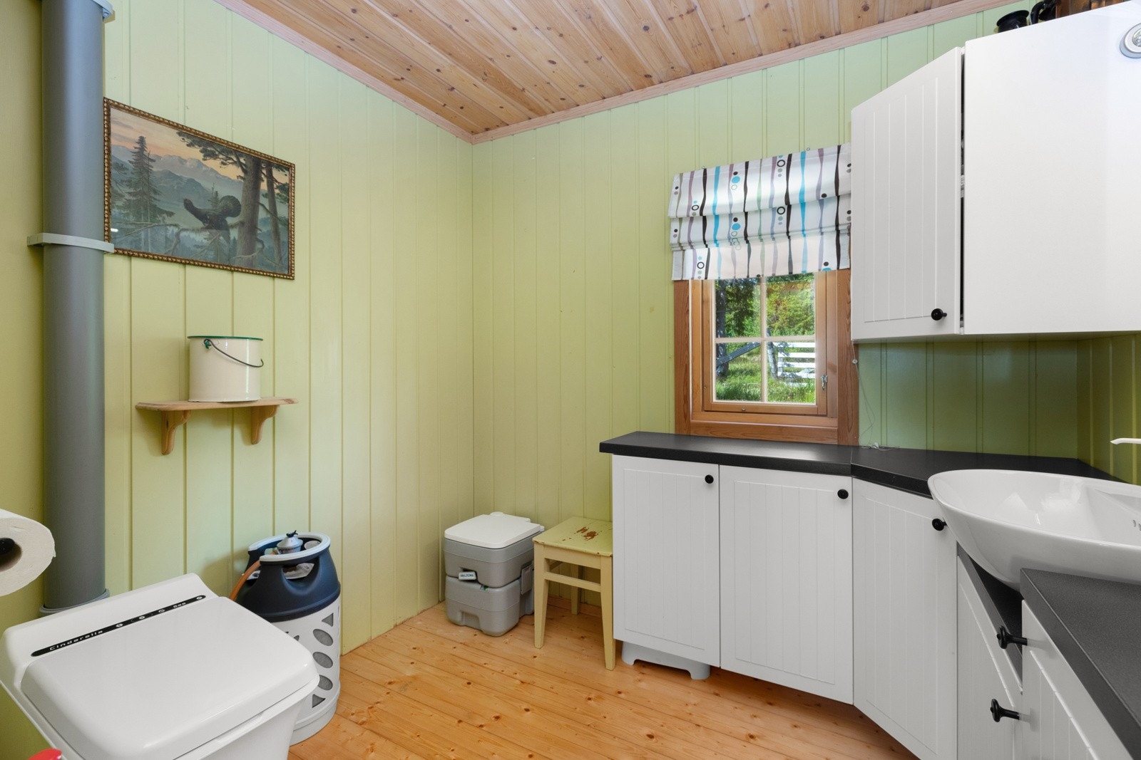 Hyttebad med forbrenningstoalett, stor innredning med god skapplass og servant plassert på benk med gråvannsavløp videre til terreng Galleribilde