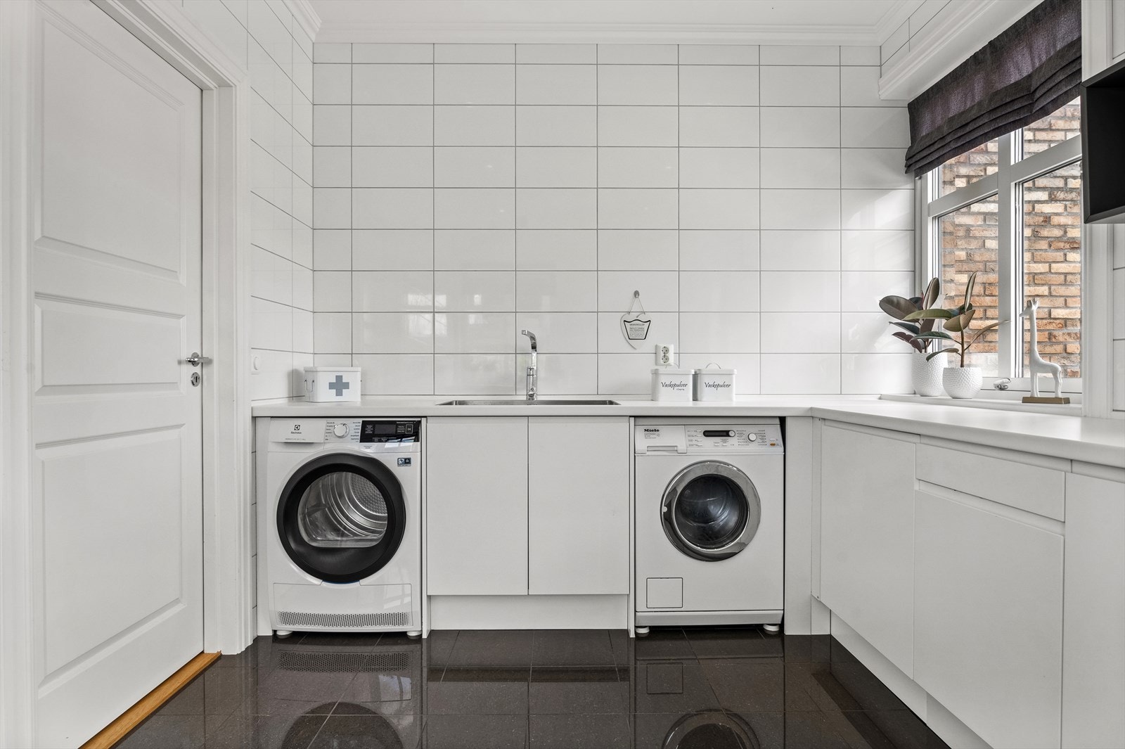 Stort praktisk vaskerom i 1. etasje med fliser på gulv og vegger. God benkeplass og laminat benkeplate med kum i rustfritt stål. Opplegg for vaskemaskin. Galleribilde