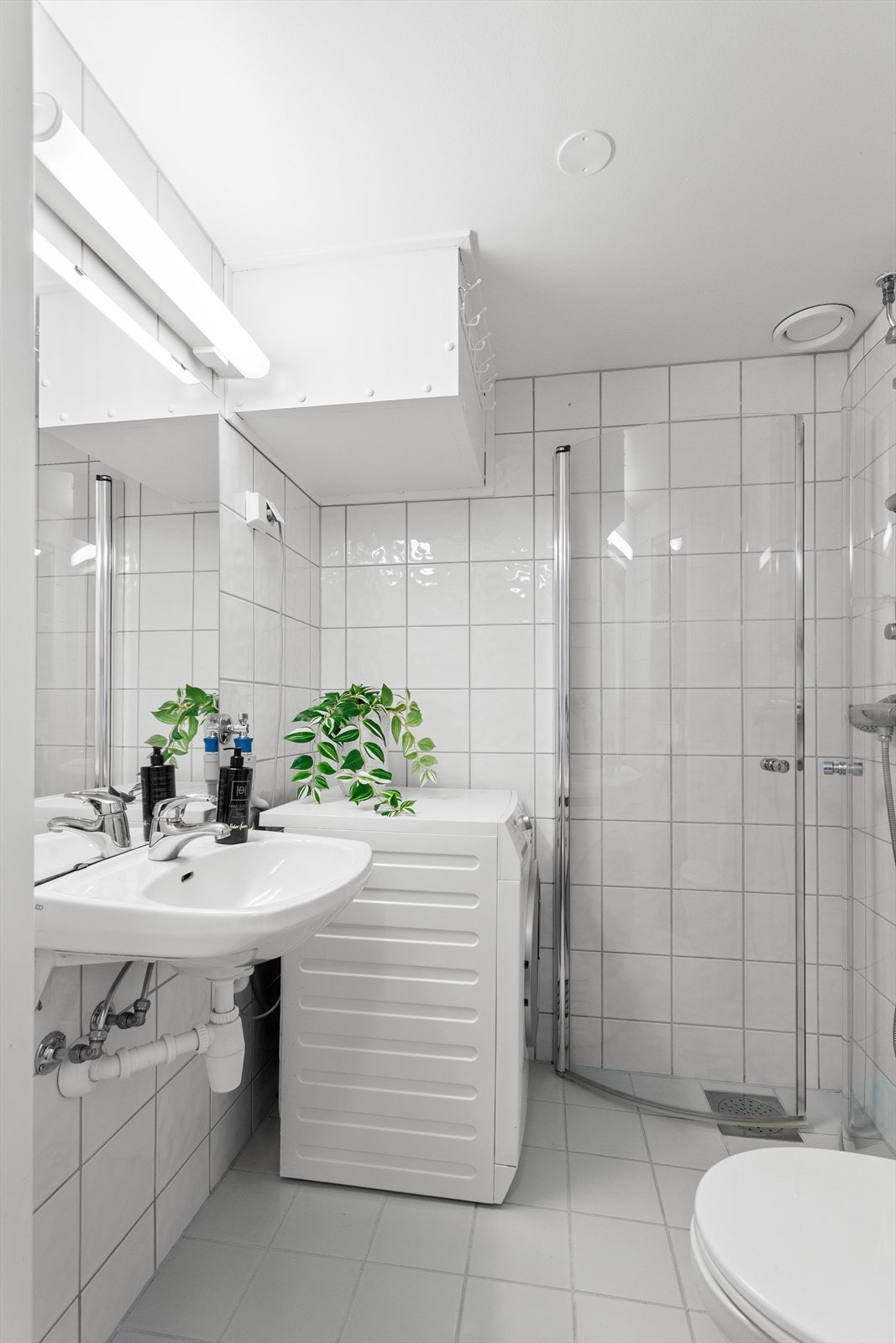 Badet har vaskemaskin og dusjhjørne med foldedører av glass Galleribilde