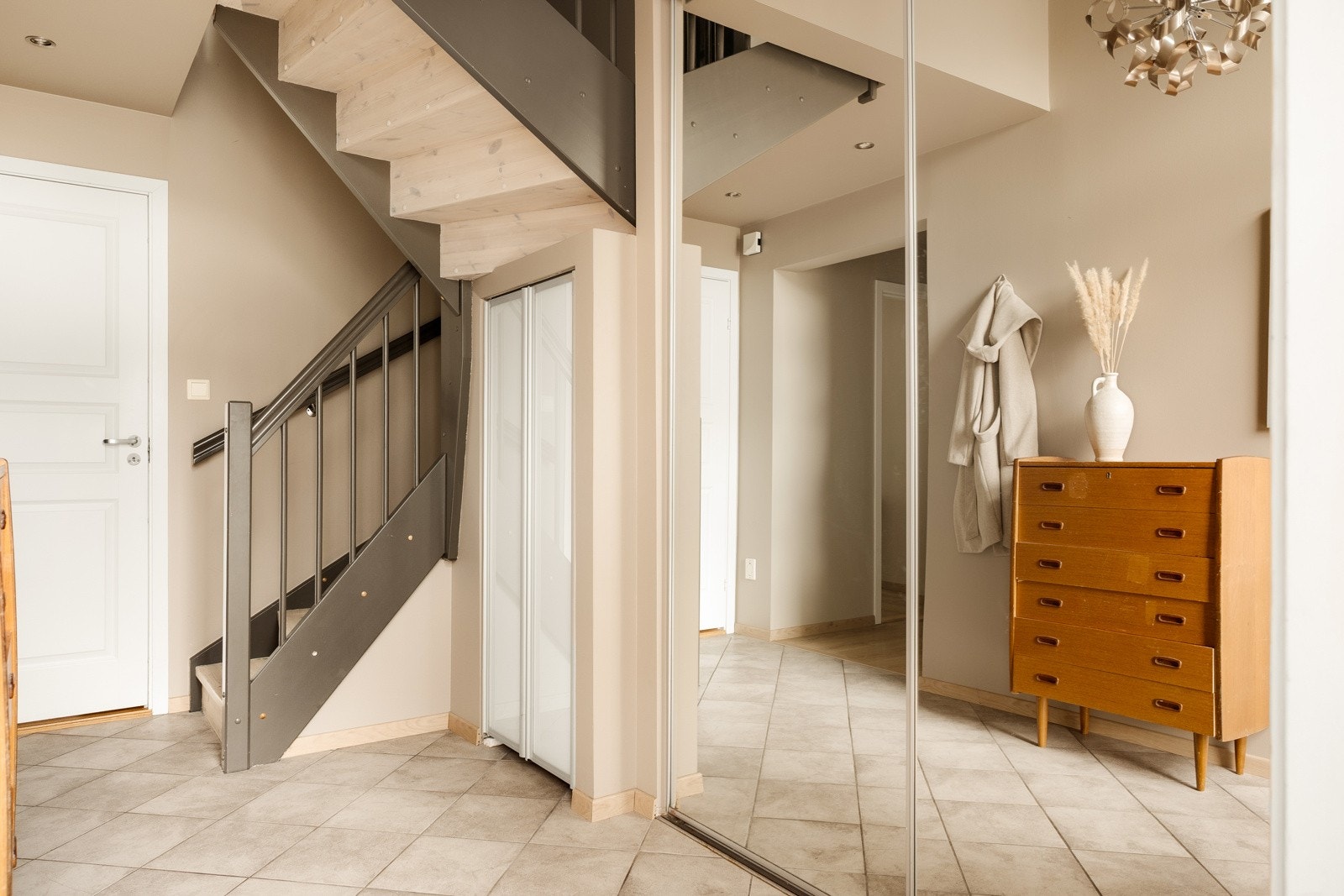 Romslig inngangsparti med praktisk skyvedørsgarderobe og ekstra lagring under trappen. Galleribilde