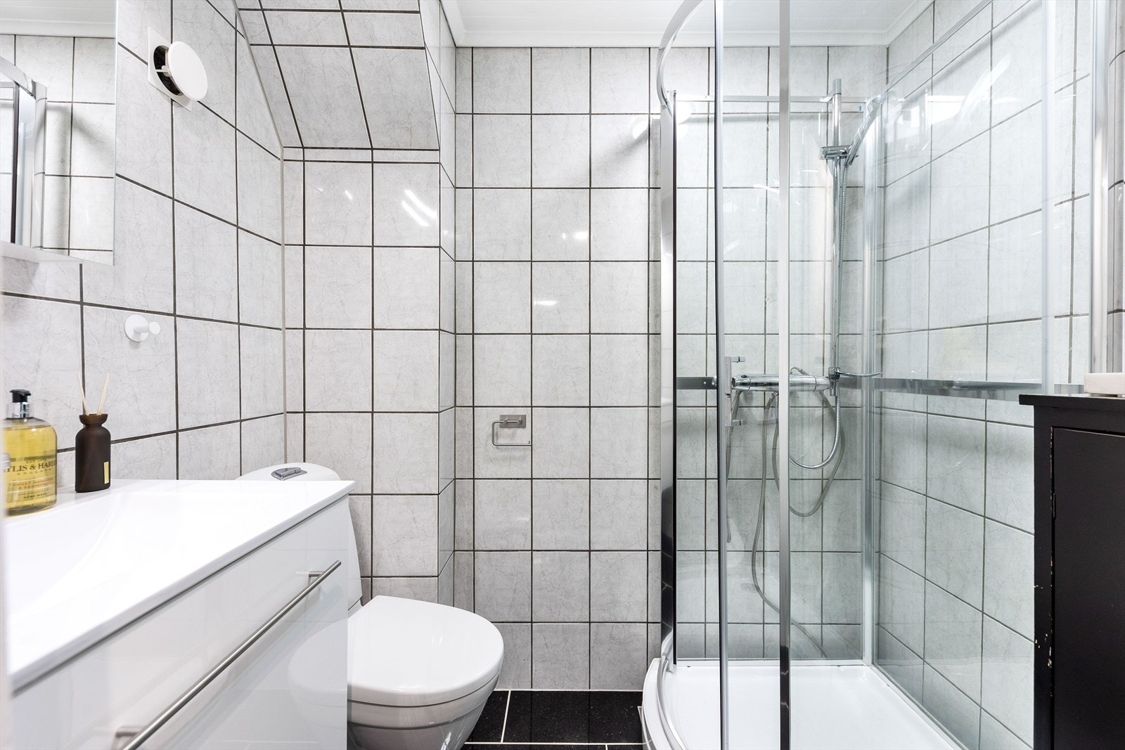 Flislagt bad utstyrt med dusjkabinett, servantskap med speil på vegg og toalett. Galleribilde