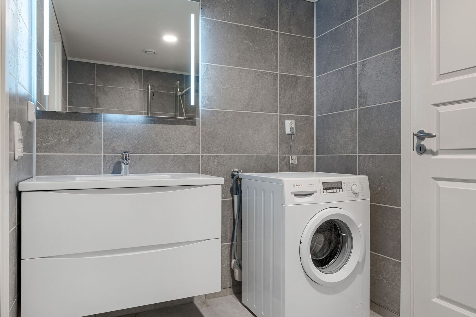 Badet er utstyrt med baderomsinnredning, dusjplass, toalett og opplegg for vaskemaskin Galleribilde