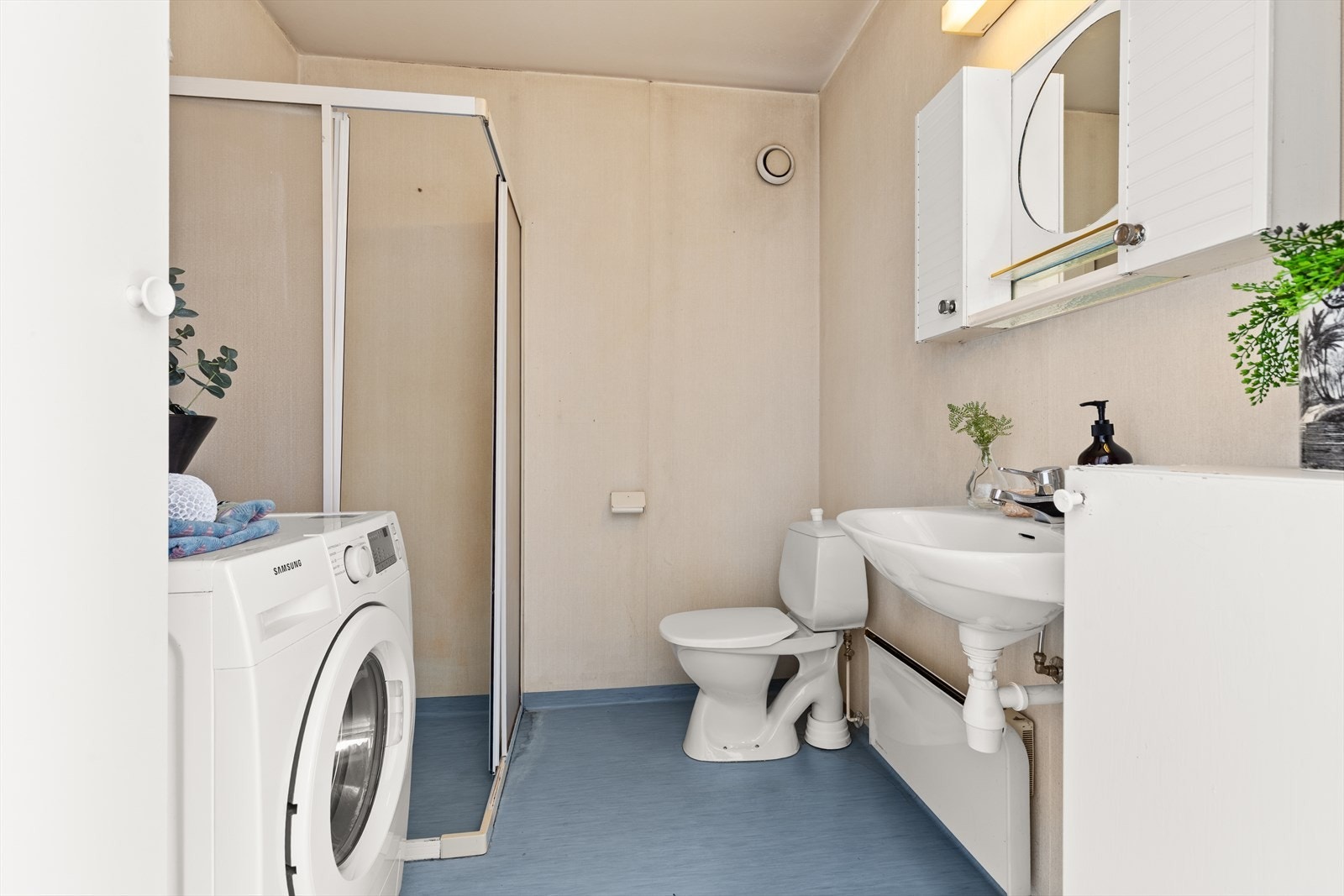 Bad med linoleum på gulv, servant med overskap, dusjkabinett på gulv og opplegg for vaskemaskin Galleribilde