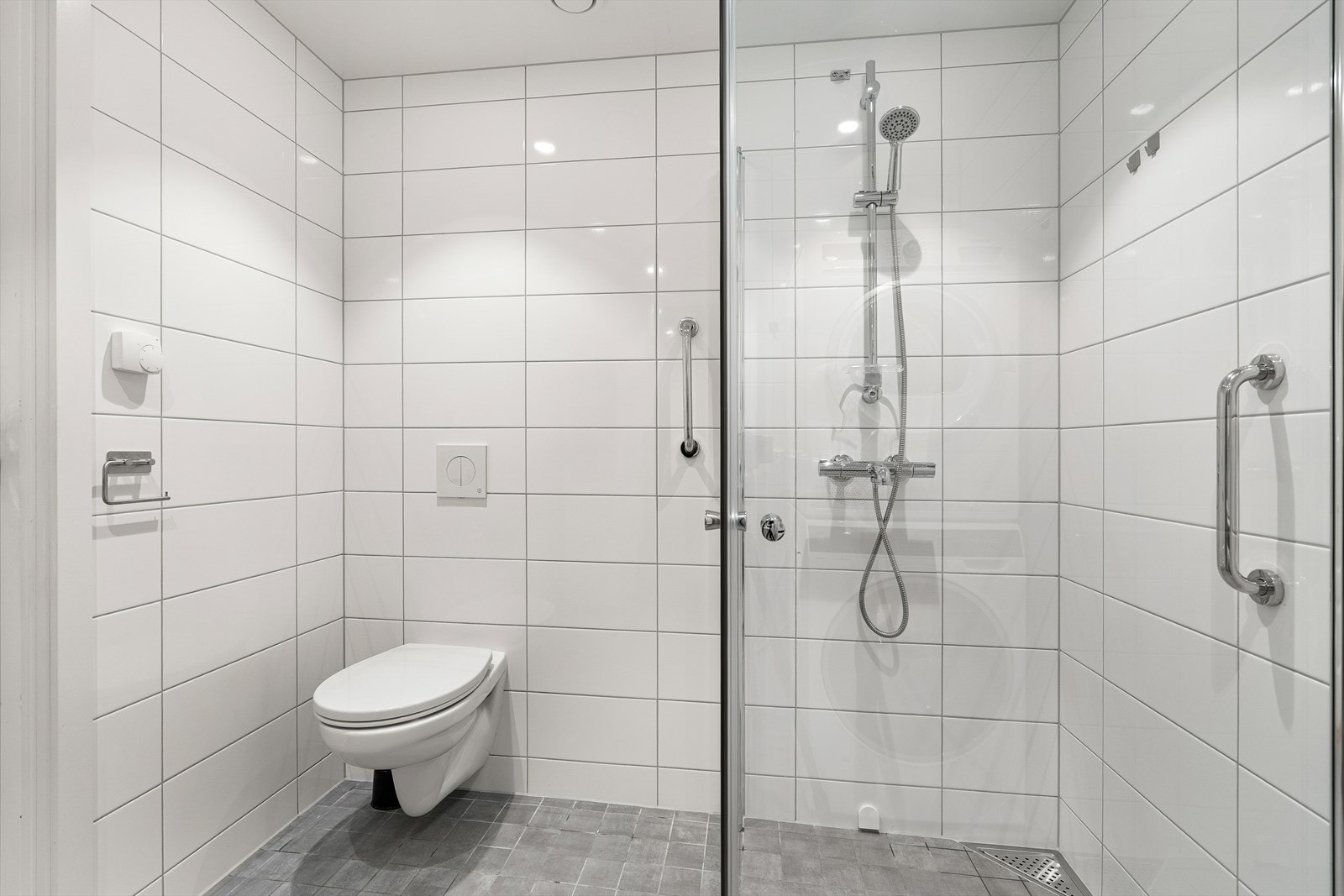 Rommet er innredet med veggmontert klosett, nedsenket vask med innredning og speil, nedsenket dusjnisje med glassdører og opplegg til vaskemaskin/tørk. Galleribilde