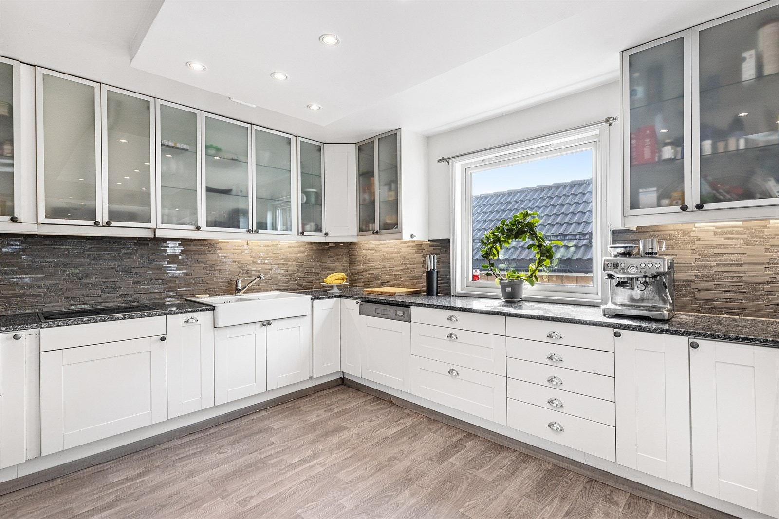 Lyst kjøkken med kjøkkeninnredning bestående av hvite, profilerte fronter og en slitesterk laminat benkeplate. Kjøkkenet har en dobbel, hvit keramikkvask utstyrt med et praktisk ettgreps blandebatteri Galleribilde