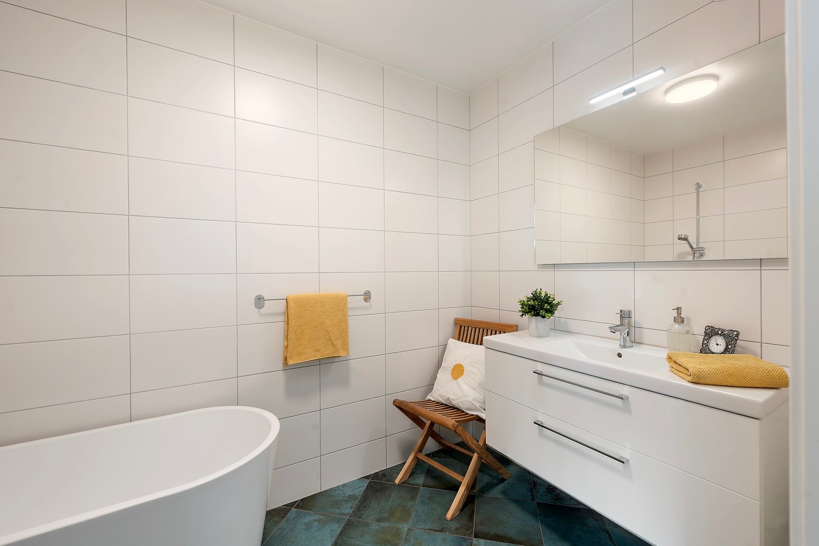 Vegg i vegg med kjøkken og soverom ligger et flislagt bad med gulvvarme, toalett, servant i innredning og badekar Galleribilde