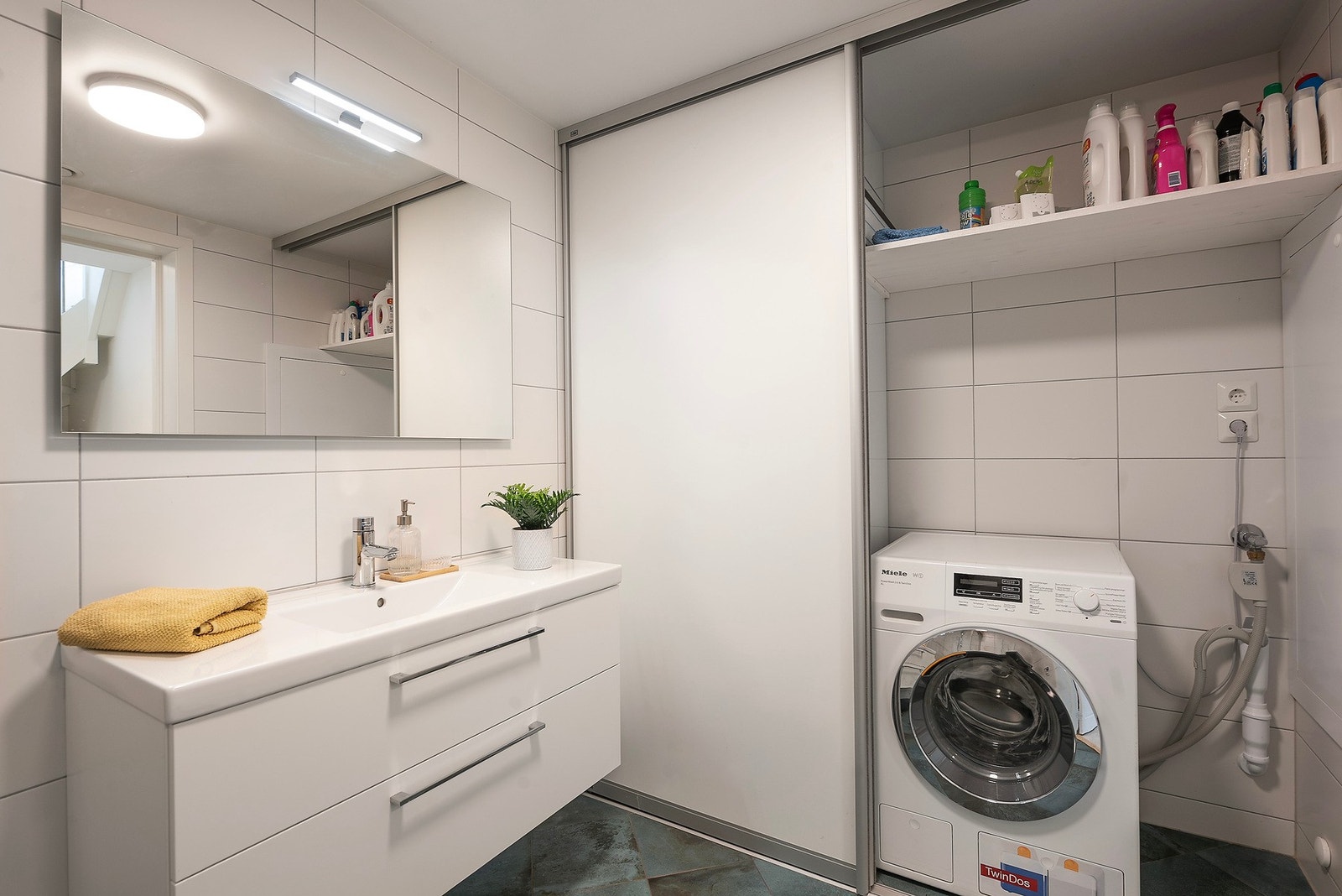 Badet i denne etasjen fungerer som et praktisk kombinasjonsrom, med opplegg for vaskemaskin og tørketrommel skjult bak skyvedører - en smart og plassbesparende løsning Galleribilde