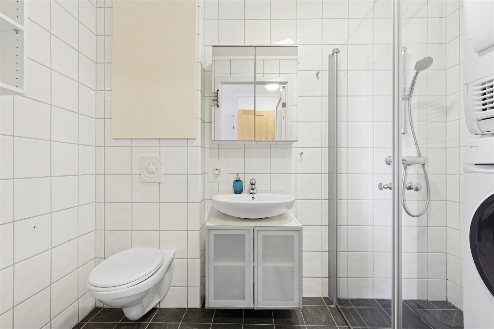 Flislagt bad i god størrelse, med moderne og praktiske løsninger som vegghengt toalett, plassbesparende dusjvegg, mekanisk avtrekk og opplegg for vaskemaskin og tørketrommel. Galleribilde