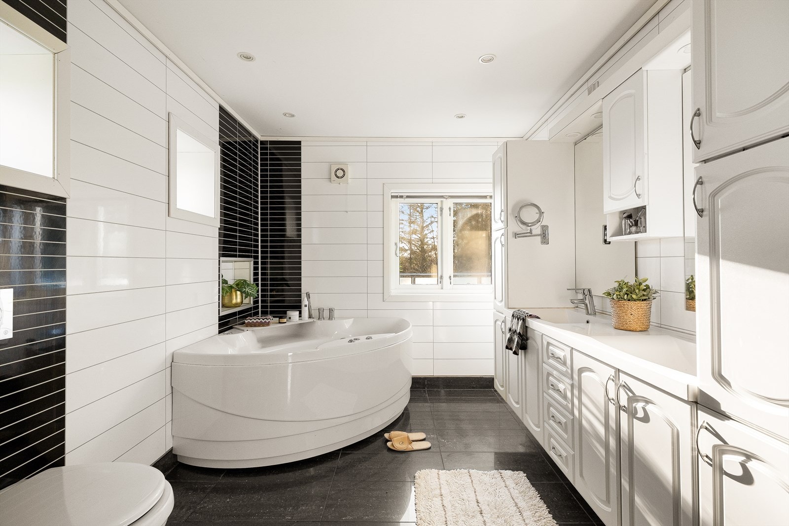 Badet i 2. etasje er ekstra romslig og har flislagt gulv med varmekabler, våtromsplater på veggene og hvitmalt tak med spotter. Det er innredet med boblebad, dusjkabinett, servant med dobbel vask og benk, langskap, overskap, speil og vegghengt toalett. Galleribilde