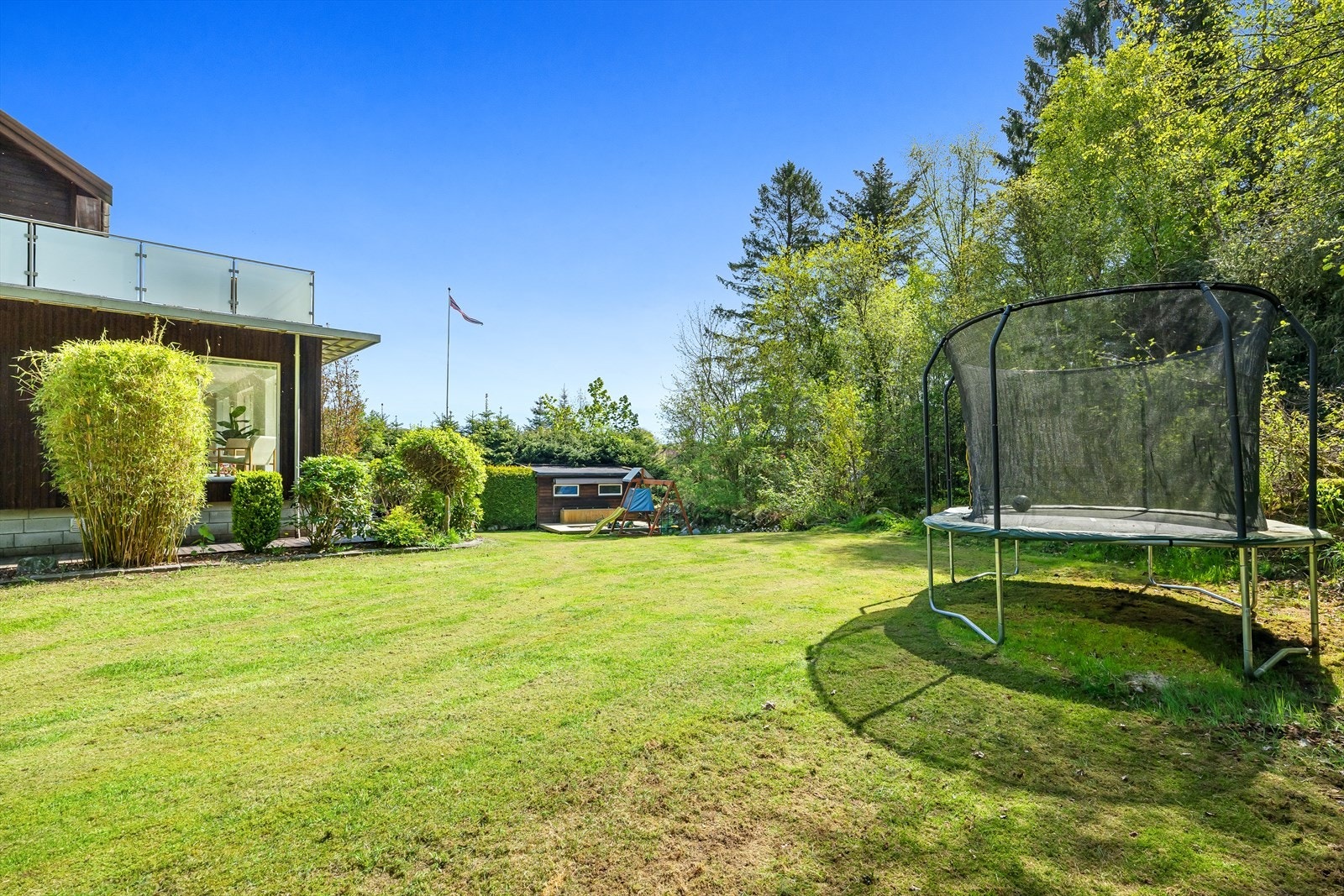 Flat og pent opparbeidet hage omringet av trær og busker. Galleribilde