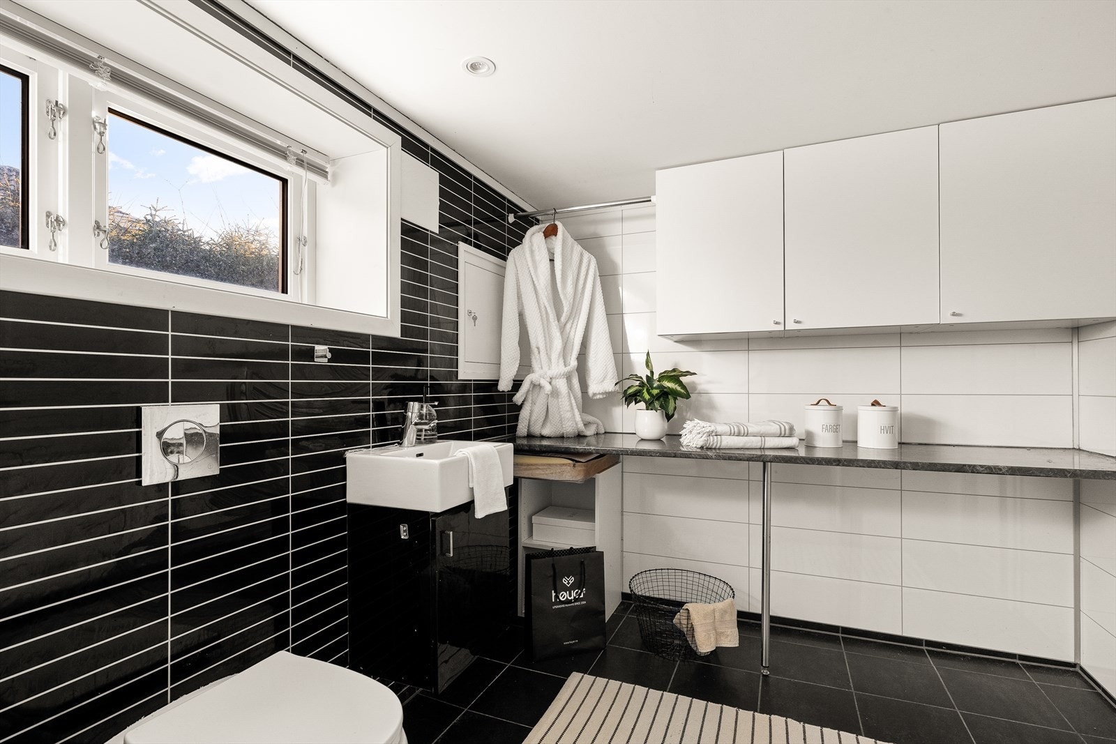 Vaskerom underetasjen har flislagt gulv med varmekabler, våtromsplater på veggene og hvitmalt tak med spotter. Det er innredet med servant i seksjon, vegghengt toalett og opplegg for vaskemaskin. En 300-liters varmtvannsbereder er plassert i dette rommet Galleribilde