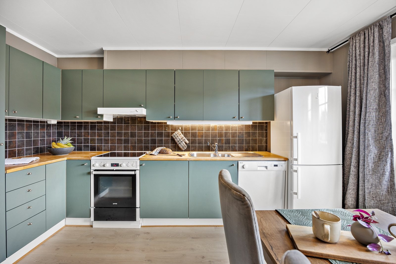 Innredningen består av grønne/glatte fronter, mørk benkeplate av tre, belysning under overskap og vask med blandebatteri. Galleribilde