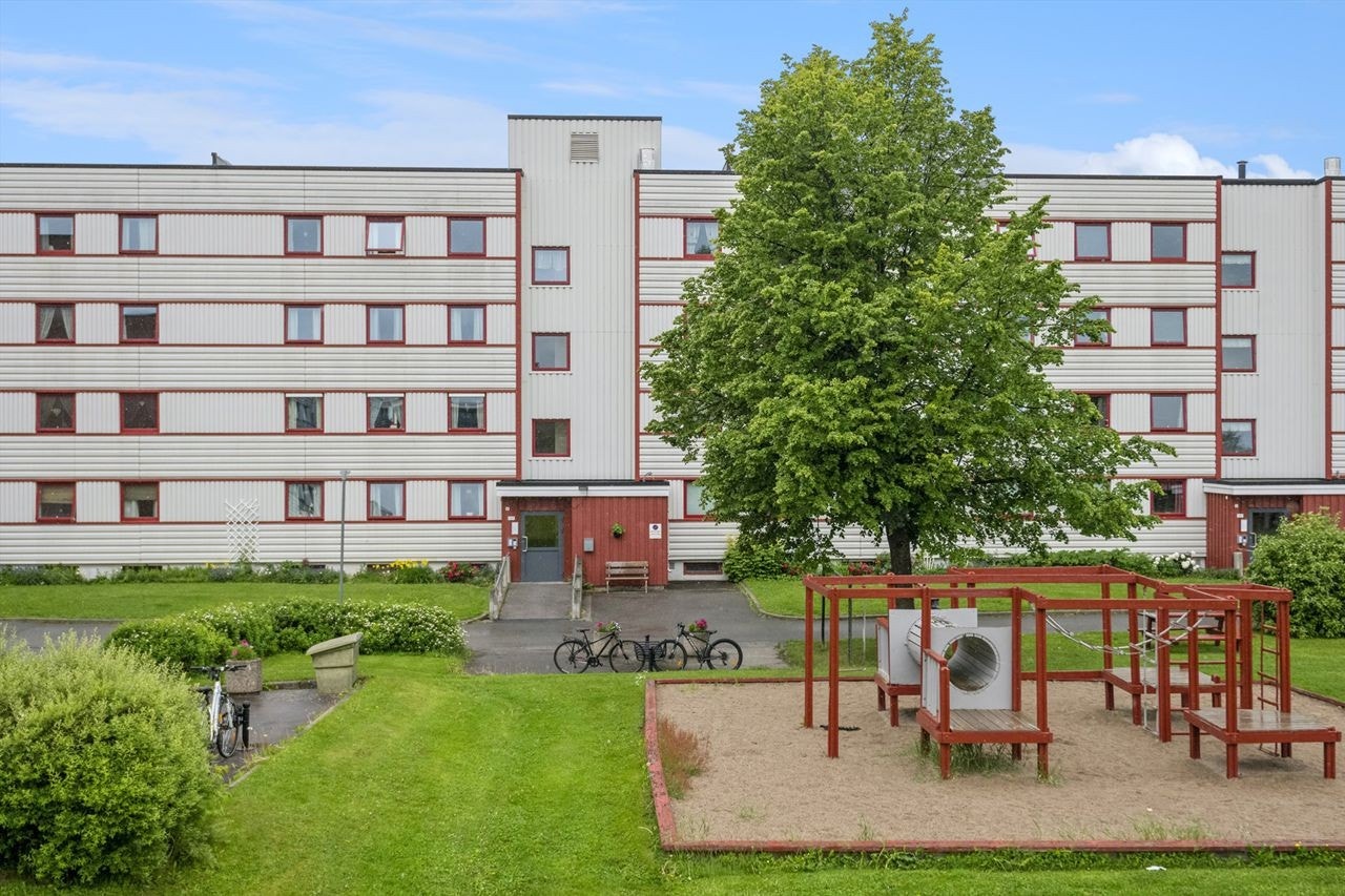Velstelt inngangsparti til boligblokken, omkranset av grønne plener og beplantning Galleribilde